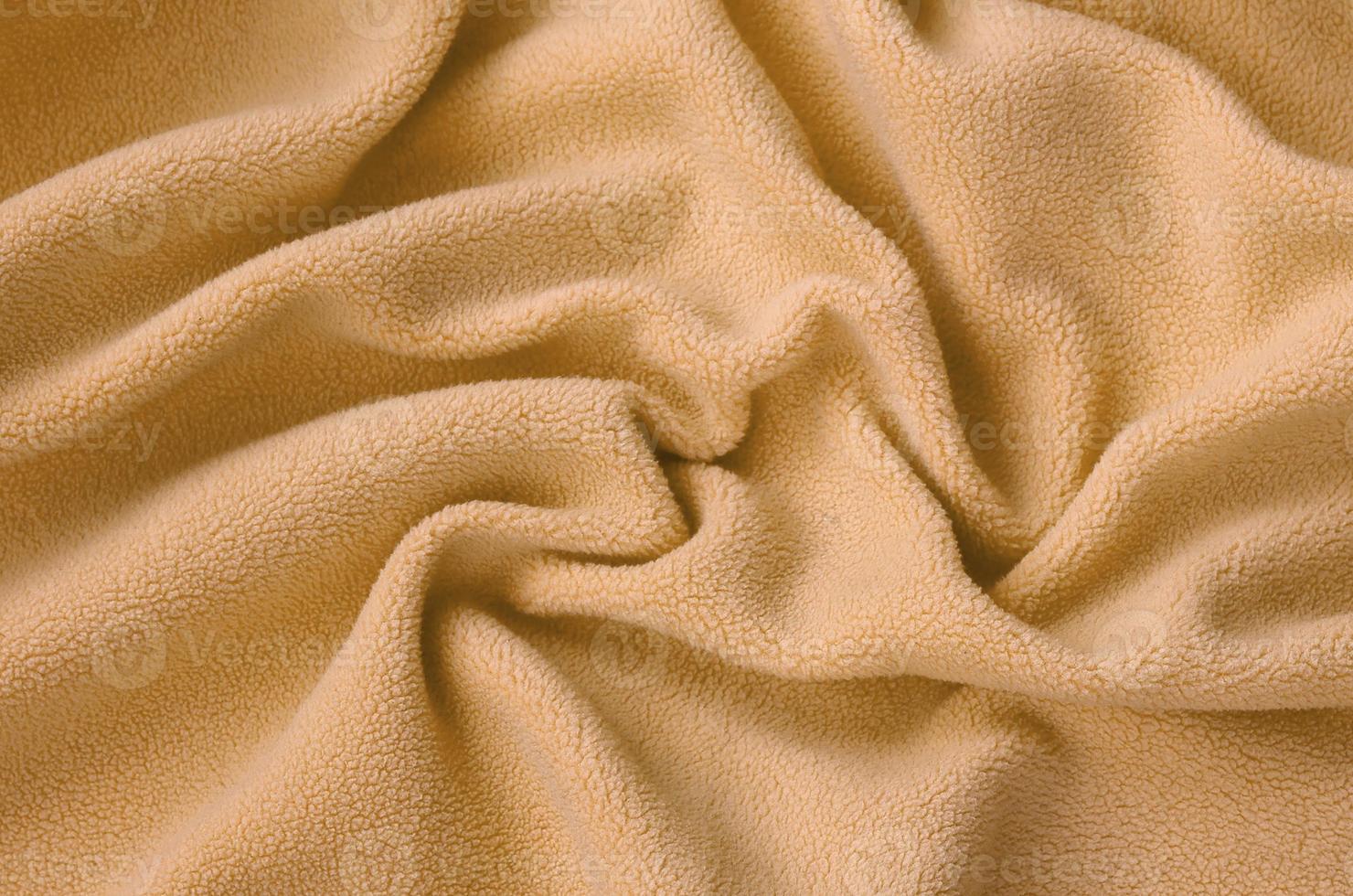The blanket of furry orange fleece fabric. A background of light orange soft plush fleece material with a lot of relief folds photo