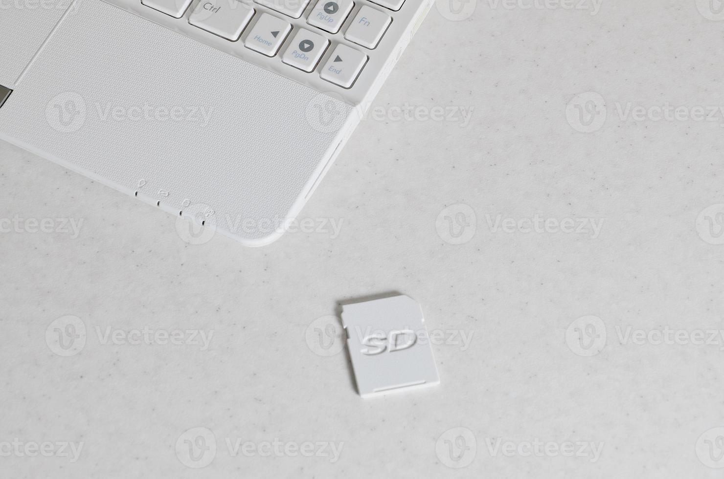 A compact SD memory card lies on a white netbook. The digital information storage device is ready for use. Concept of modern technologies photo