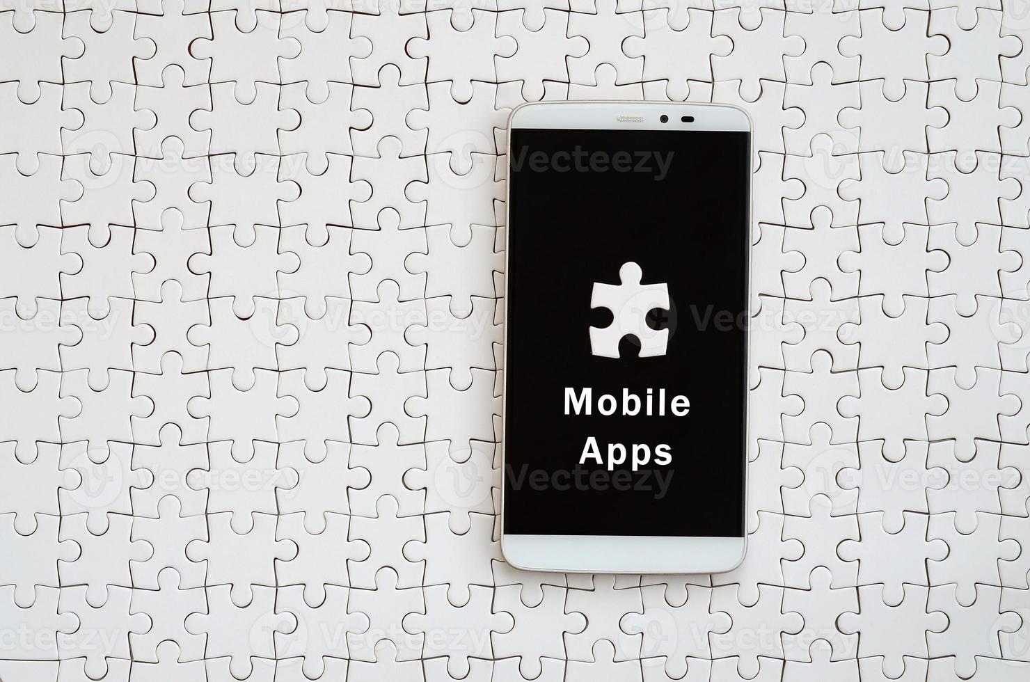 A modern big smartphone with a touch screen lies on a white jigsaw puzzle in an assembled state with inscription. Mobile apps photo