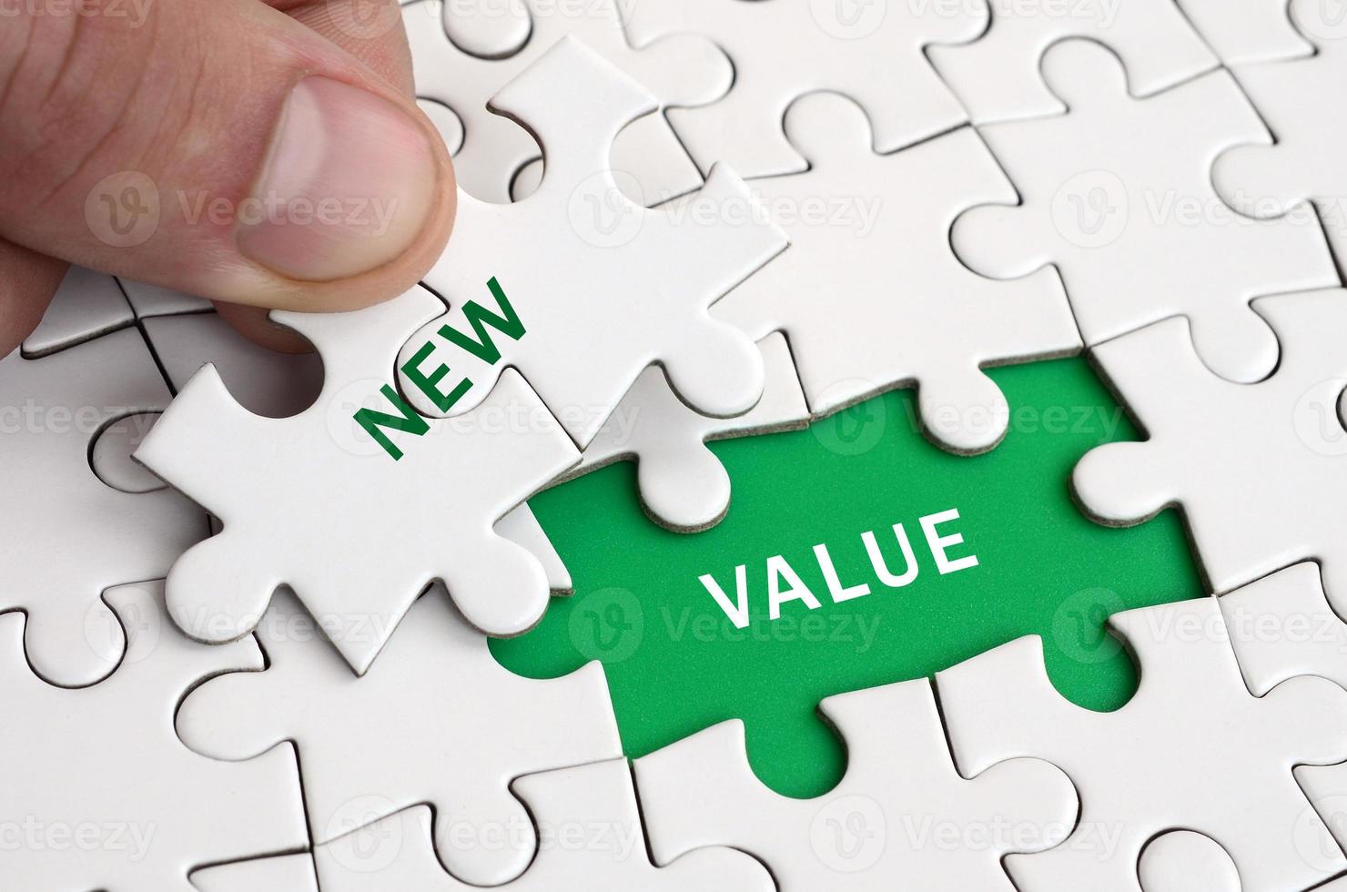 The human hand fills the last missing elements of the surface from the jigsaw puzzle. Image with words new and value photo