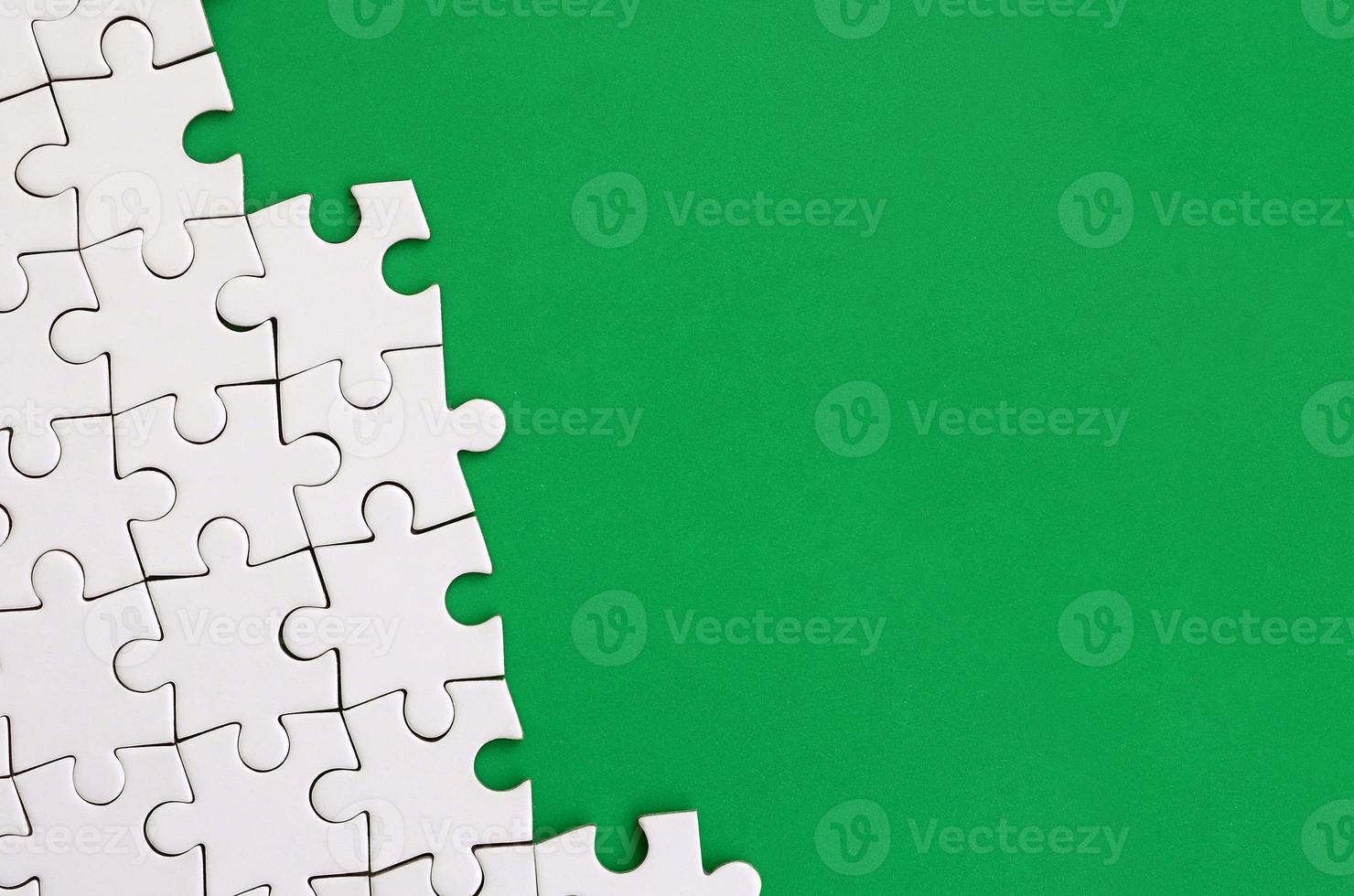 Fragment of a folded white jigsaw puzzle on the background of a green plastic surface. Texture photo with copy space for text