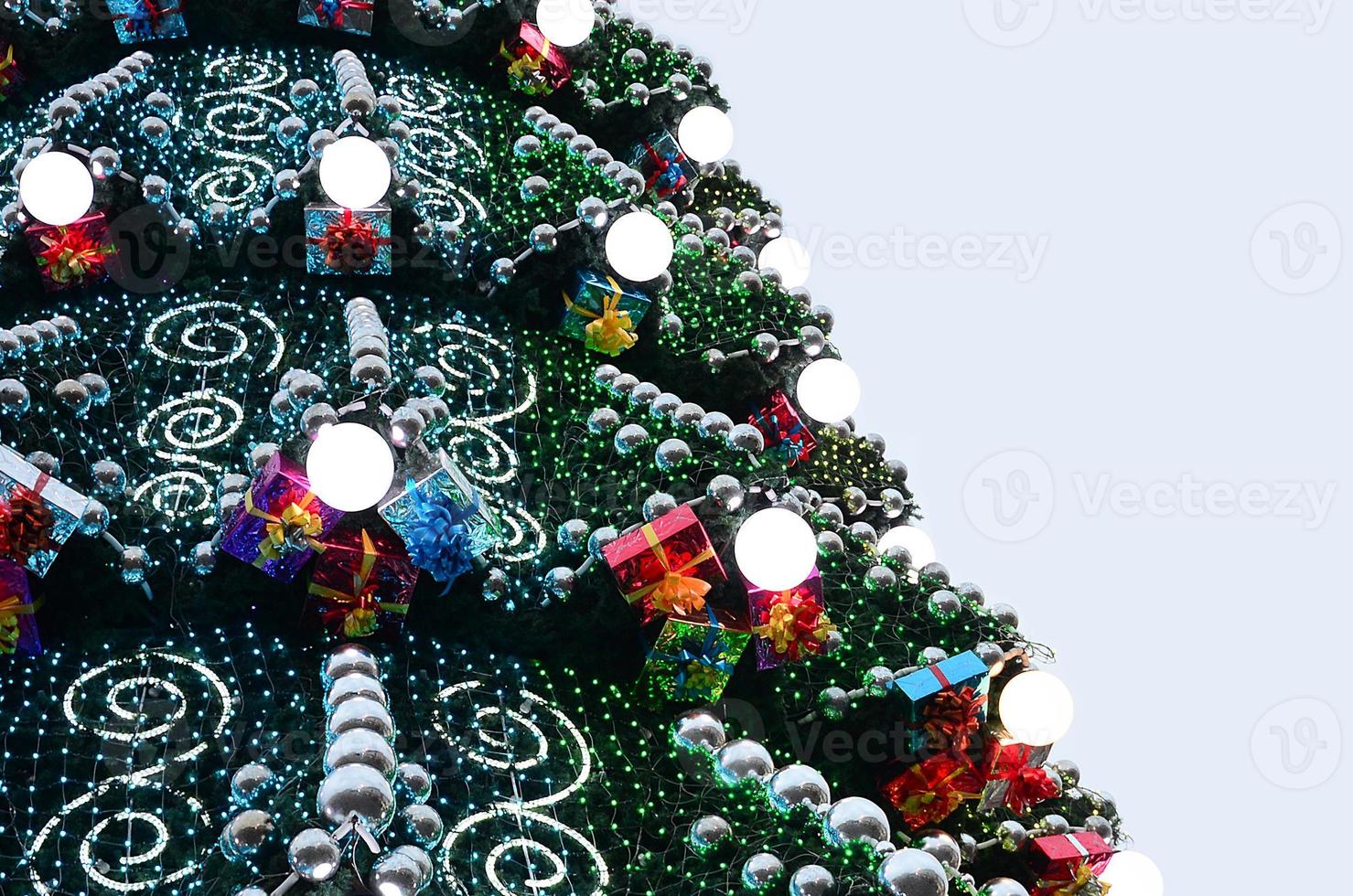 A fragment of a huge Christmas tree with many ornaments, gift boxes and luminous lamps. Photo of a decorated Christmas tree close-up with copy space