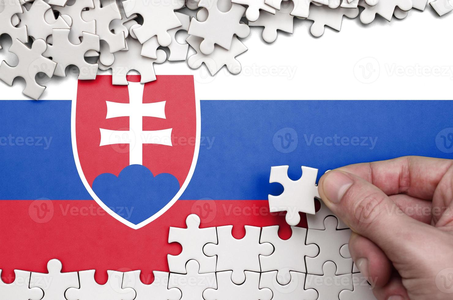 Slovakia flag is depicted on a table on which the human hand folds a puzzle of white color photo