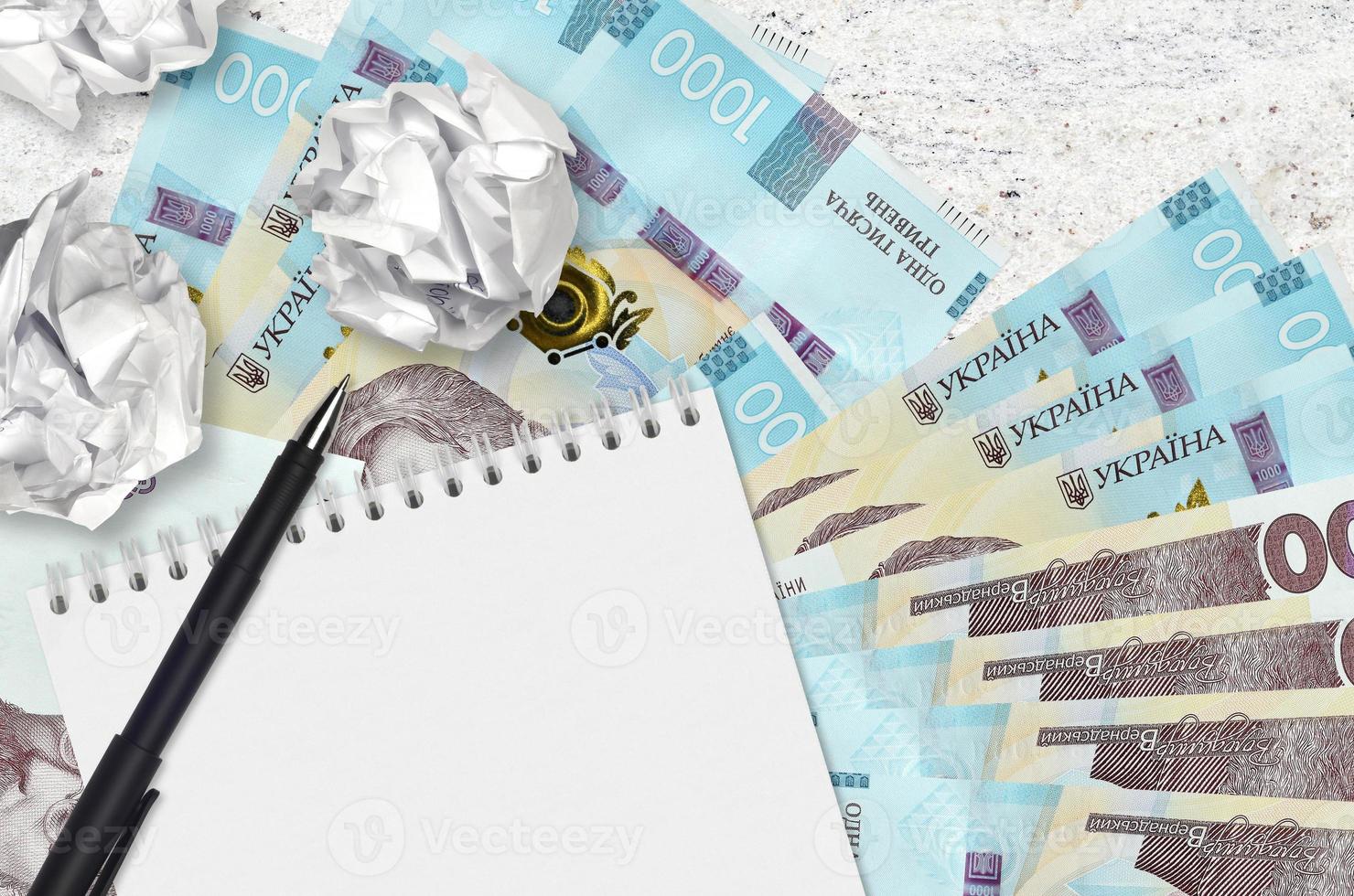 1000 Ukrainian hryvnias bills and balls of crumpled paper with blank notepad. Bad ideas or less of inspiration concept. Searching ideas for investment photo