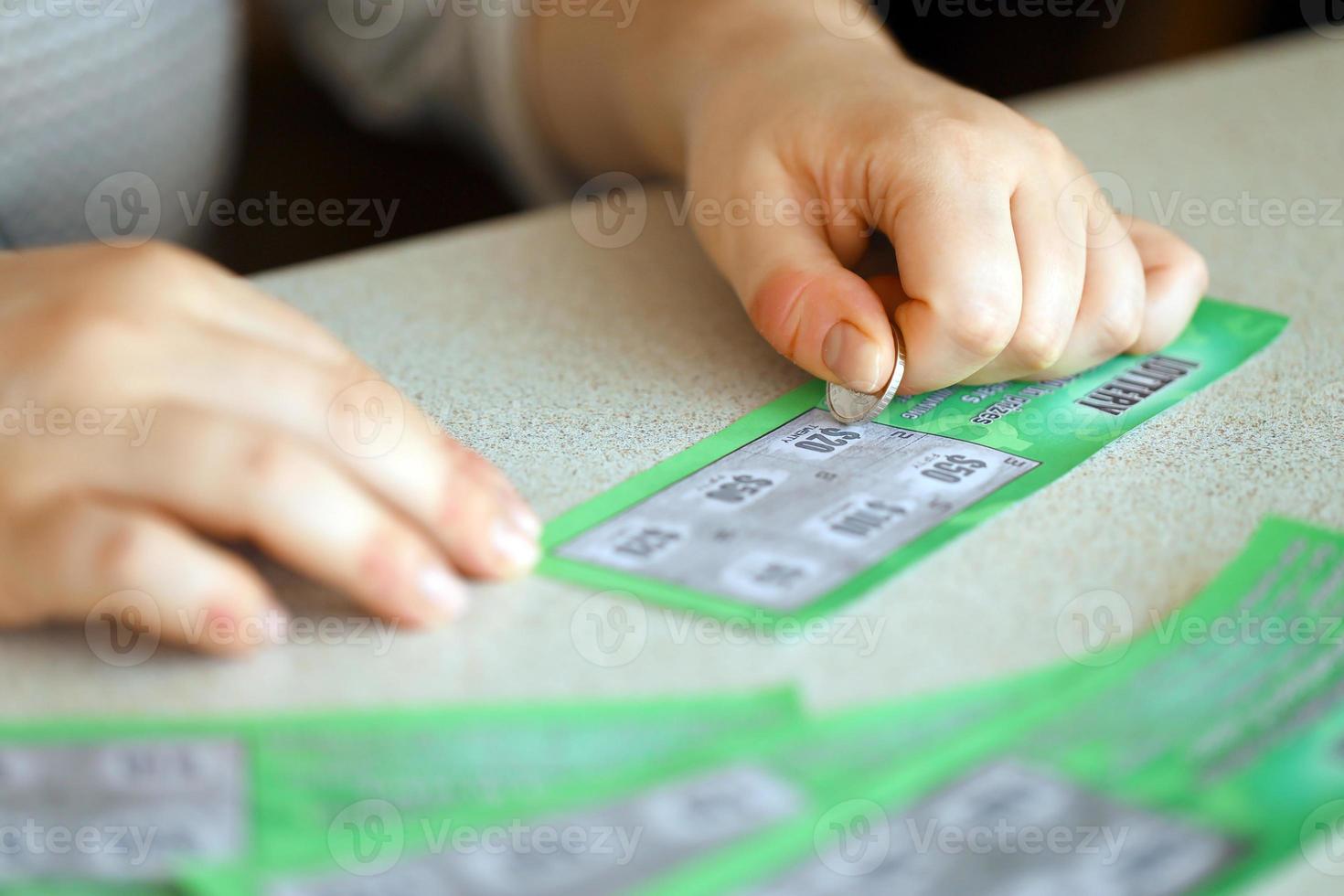 Close up view of silver coin in hand of gambler scratching fake lottery card. Lottery gambling concept, scratching cards lottery photo