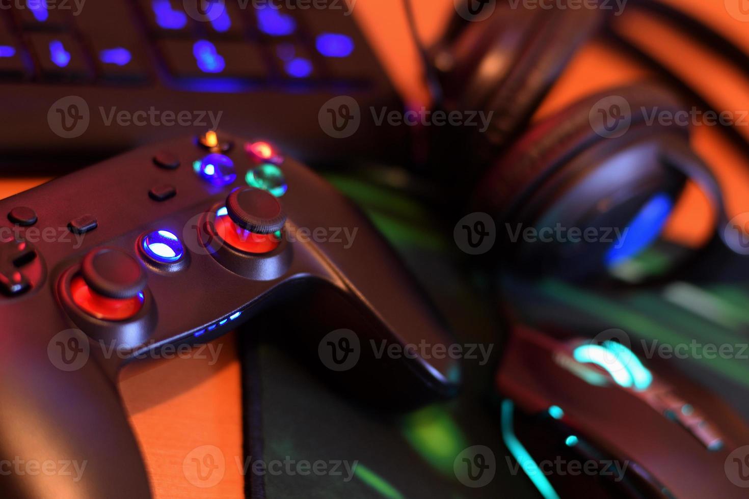 Modern gamepad and gaming mouse lies with keyboard and headphones on table in dark playroom scene. Video gaming addiction among teenagers concept photo