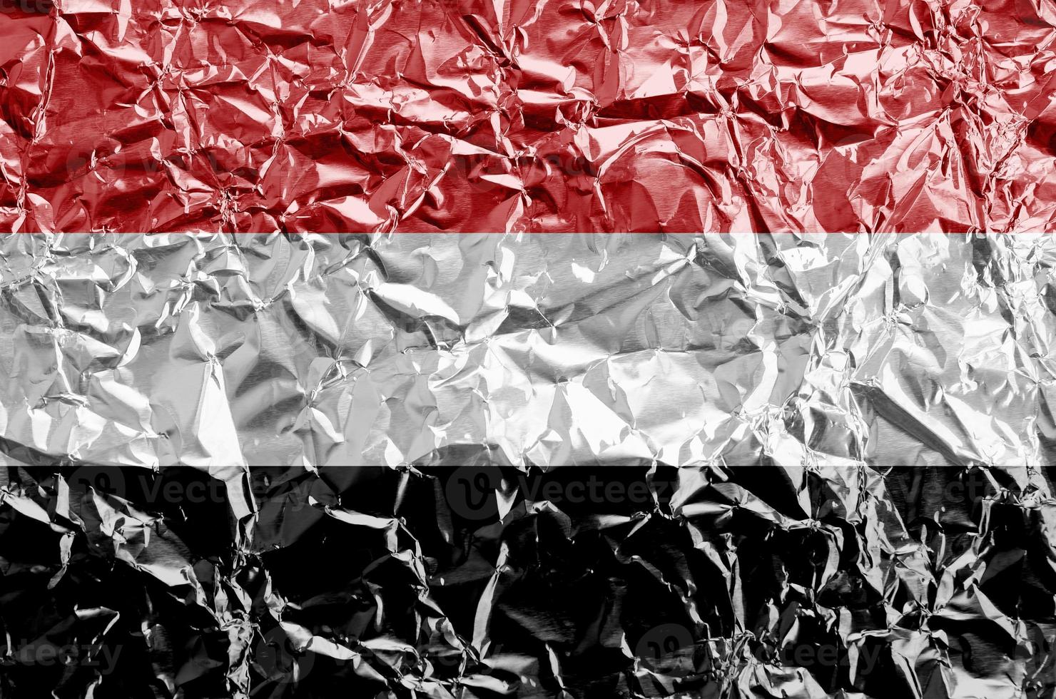 Yemen flag depicted in paint colors on shiny crumpled aluminium foil closeup. Textured banner on rough background photo