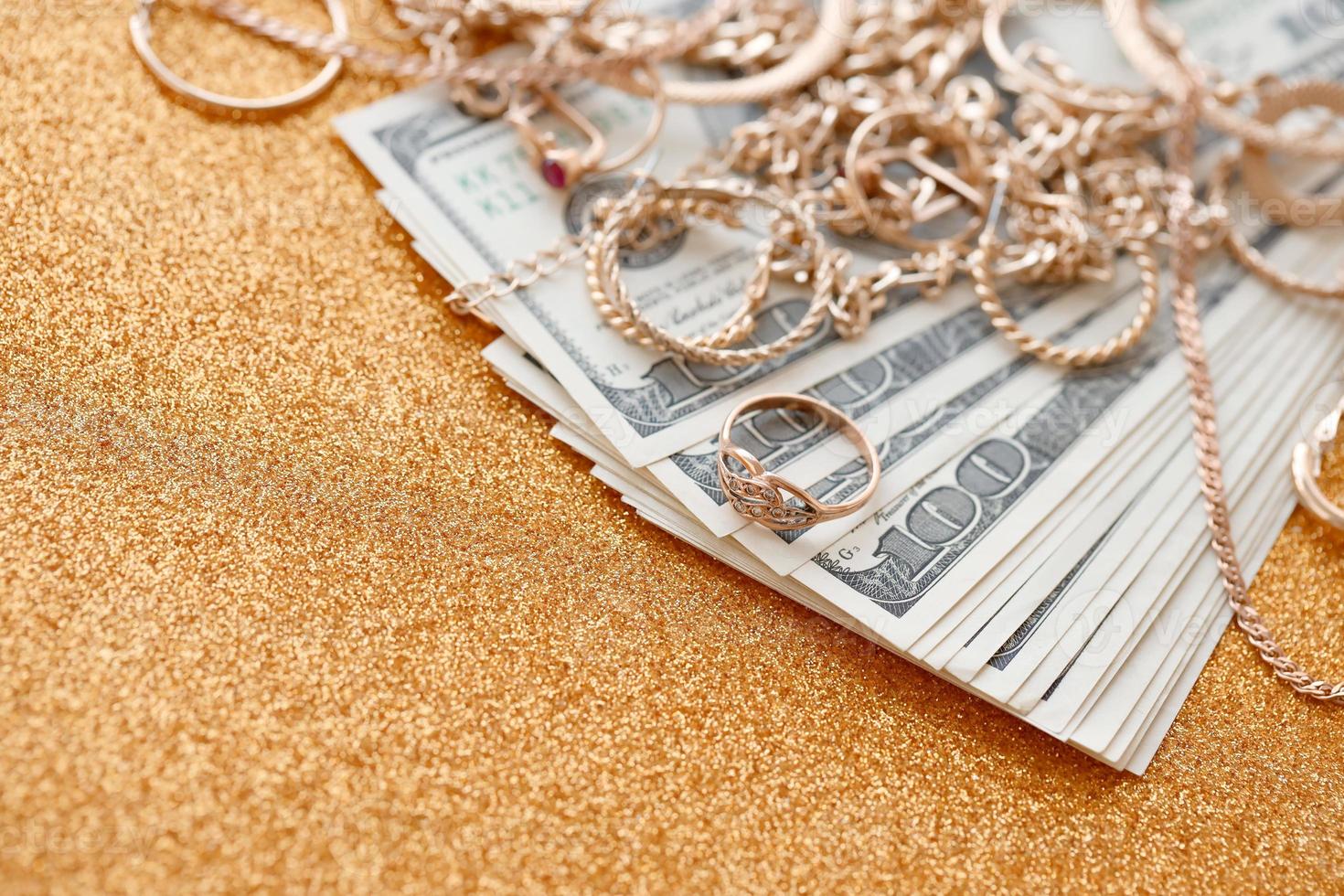 Many expensive golden jewerly rings, earrings and necklaces with big amount of US dollar bills on luxury glitter golden background surface. Pawnshop or jewerly shop photo