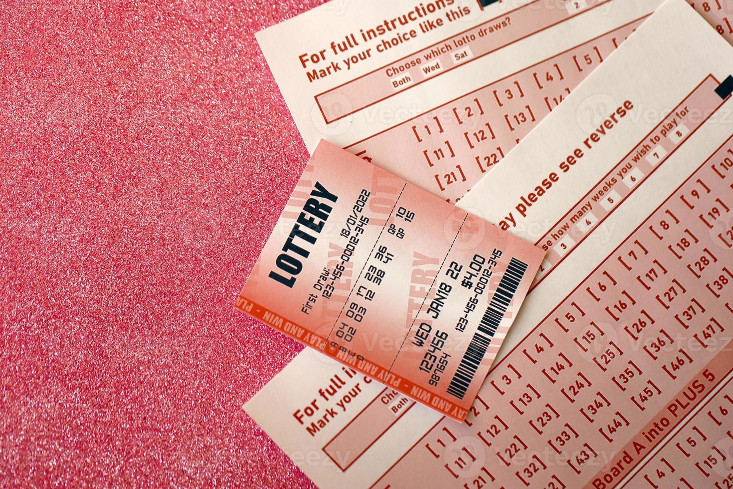 Red lottery ticket lies on pink gambling sheets with numbers for marking to play lottery. Lottery playing concept or gambling addiction. Close up photo