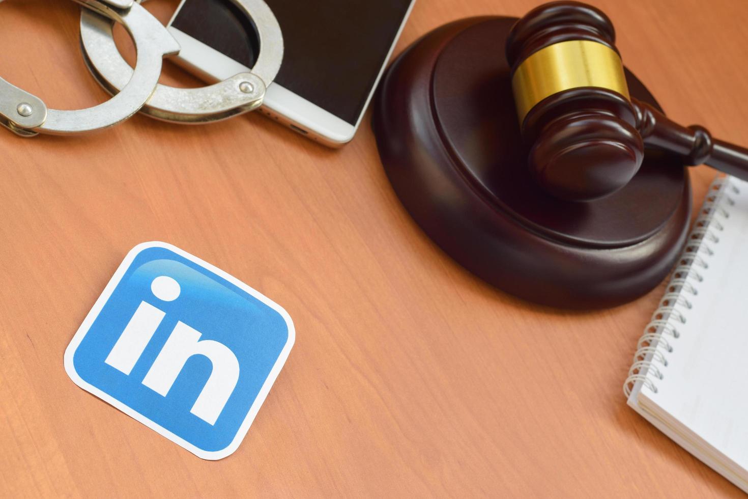 KHARKOV, UKRAINE - MAY 3, 2022 Linkedin paper logo lies with wooden judge gavel, smartphone and handcuffs. Entertainment lawsuit concept photo