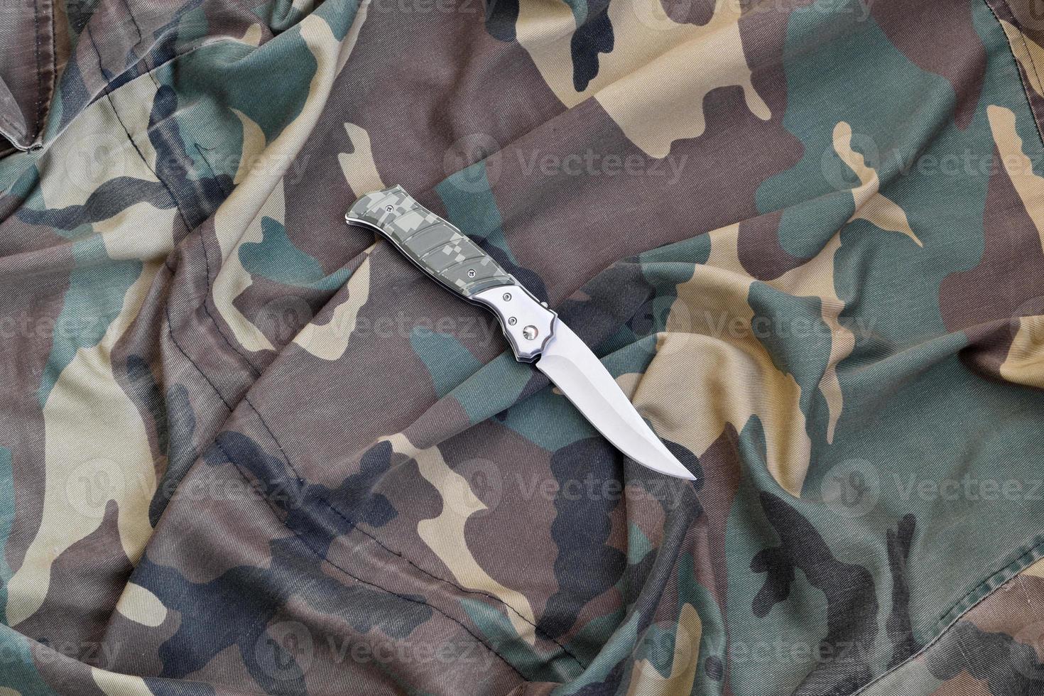 Military knife on army camouflage clothes close up. Background with copy space for military or special service design photo