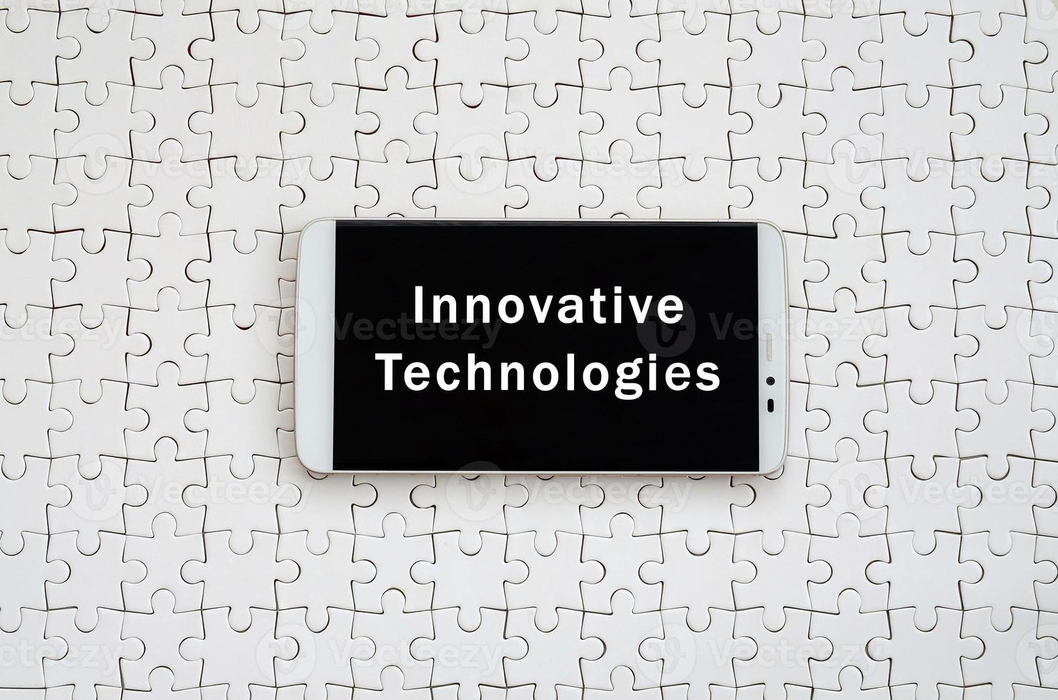 A modern big smartphone with a touch screen lies on a white jigsaw puzzle in an assembled state with inscription. Innovative technologies photo
