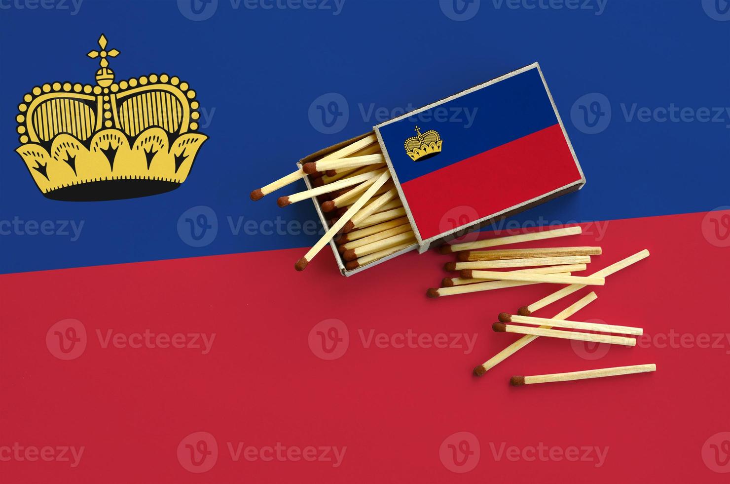 Liechtenstein flag is shown on an open matchbox, from which several matches fall and lies on a large flag photo