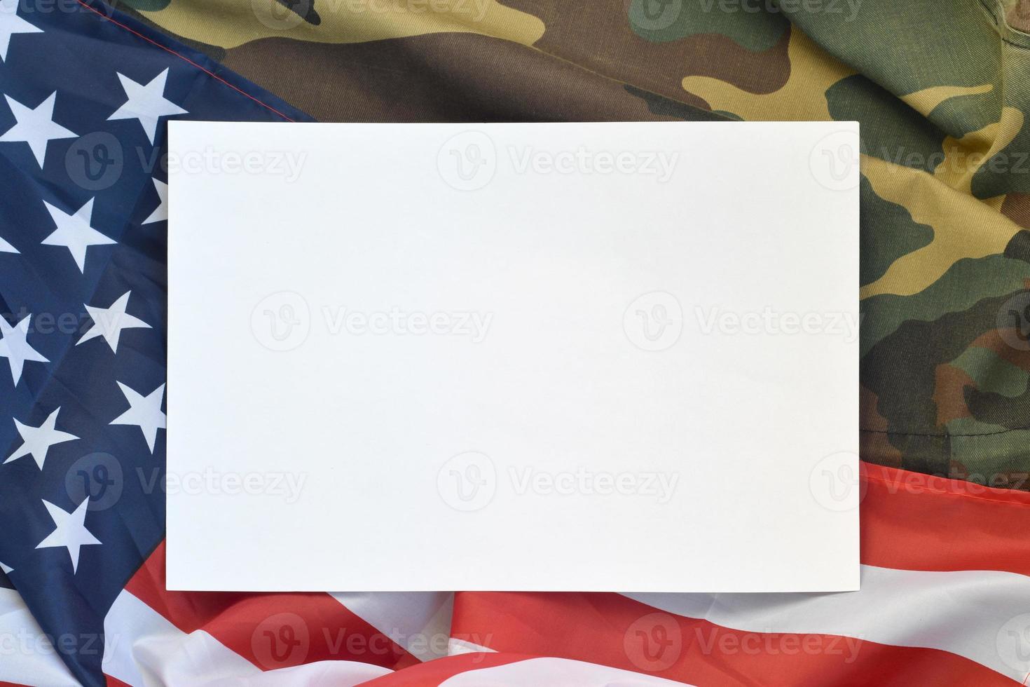 Blank paper lies on United States of America flag and folded military uniform jacket. Military symbols conceptual background banner and copy space photo