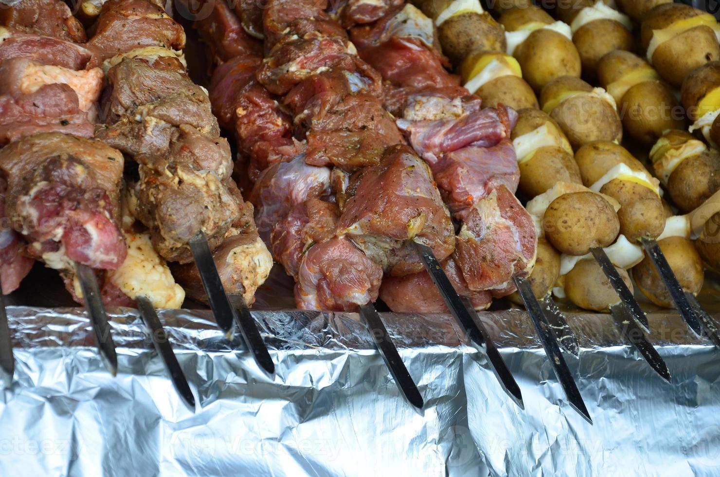 la carne cruda y las patatas se plantan en brochetas de metal. el proceso de cocinar shish kebabs. comida de campamento rusa y ucraniana foto