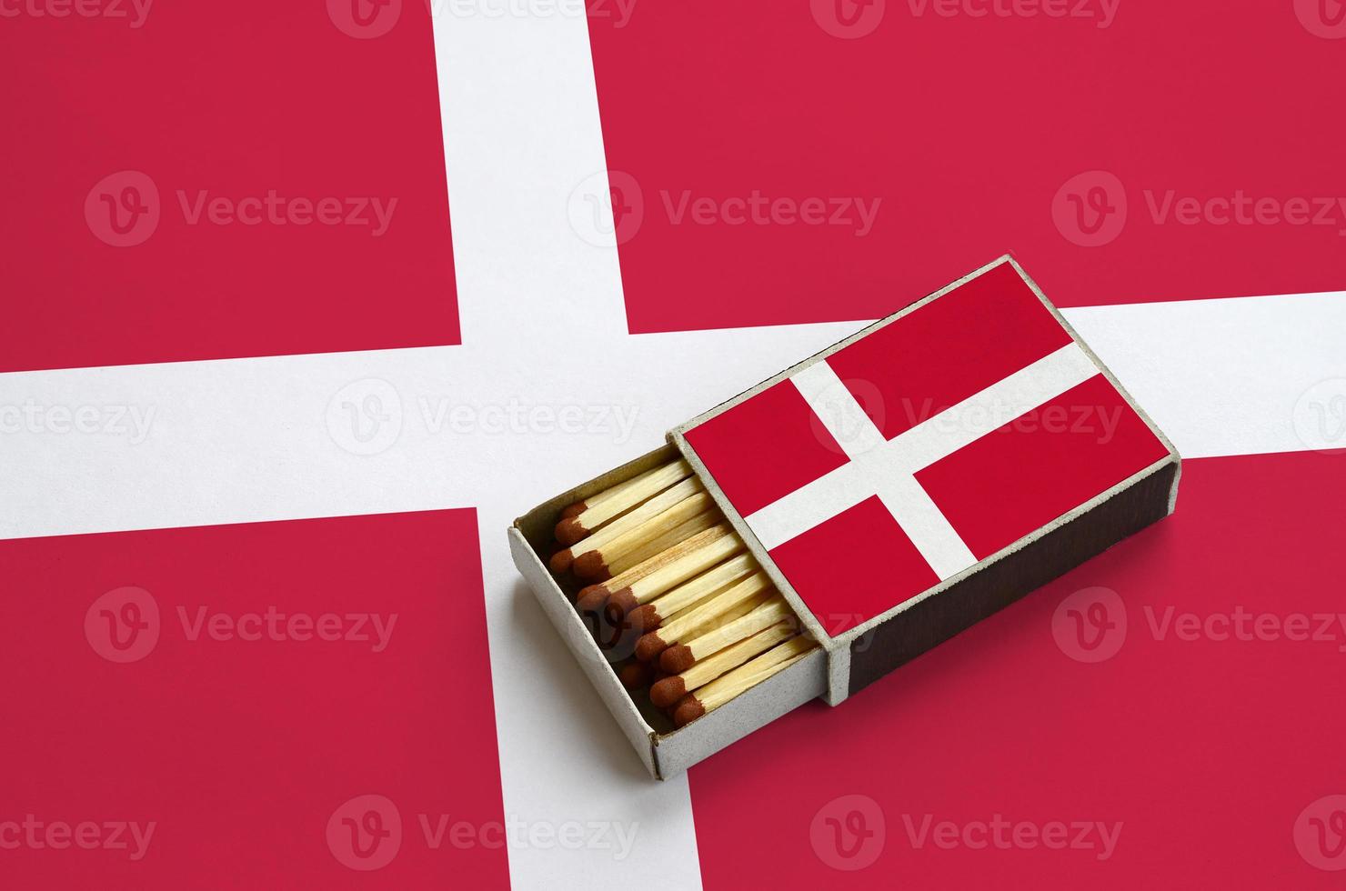 Denmark flag is shown in an open matchbox, which is filled with matches and lies on a large flag photo