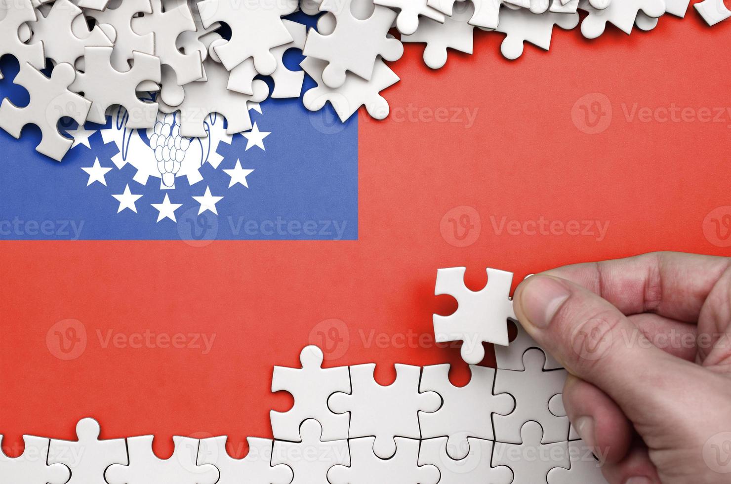 Myanmar flag is depicted on a table on which the human hand folds a puzzle of white color photo