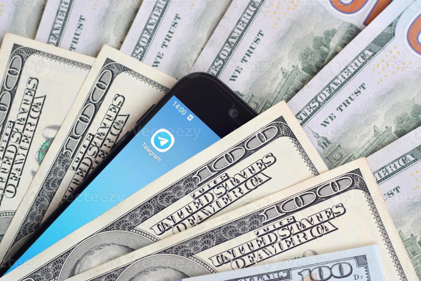 Smartphone screen with Telegram app and lot of hundred dollar bills. Business and social networking concept photo