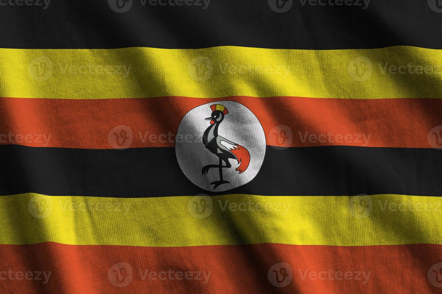 Uganda flag with big folds waving close up under the studio light indoors. The official symbols and colors in banner photo