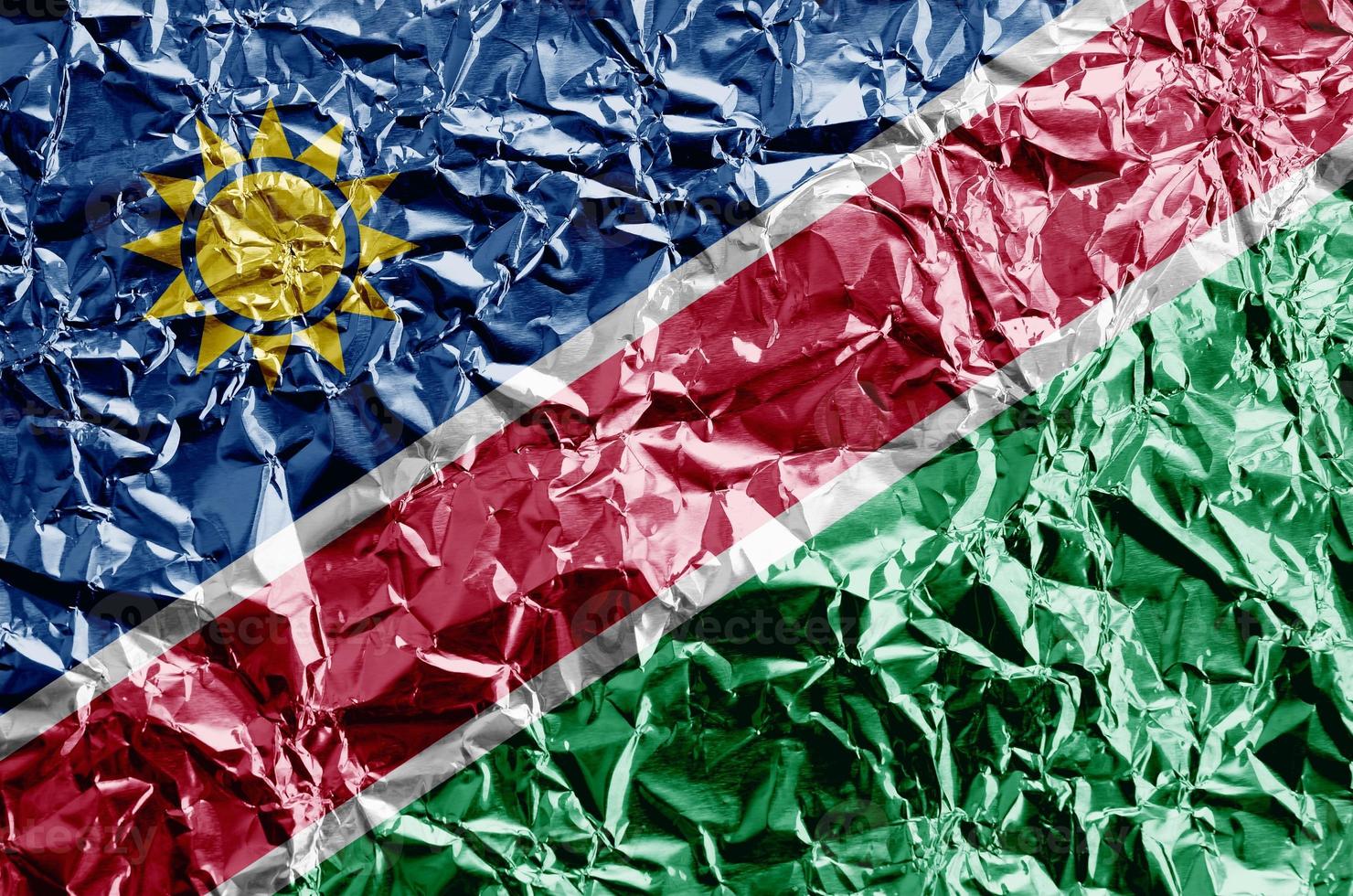 Namibia flag depicted in paint colors on shiny crumpled aluminium foil closeup. Textured banner on rough background photo