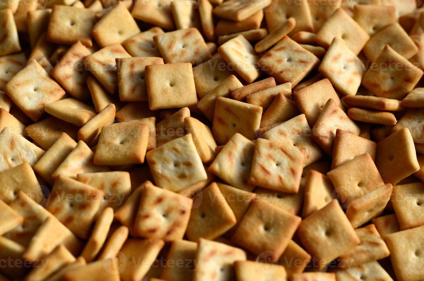 A lot of small cookies are square shaped. A pattern of a yellow salt cracker. Background image with salted pastry photo