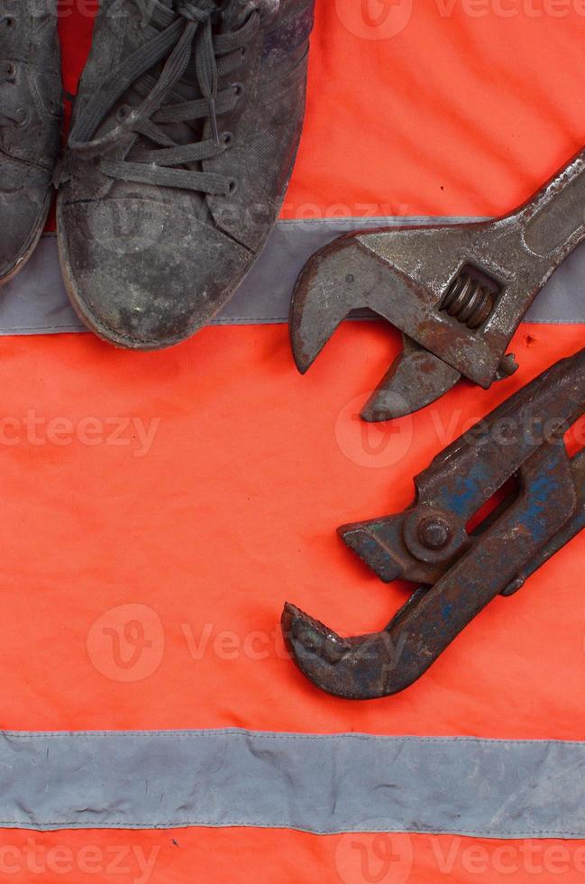 Adjustable wrenches and old boots lies on an orange signal worker shirt photo