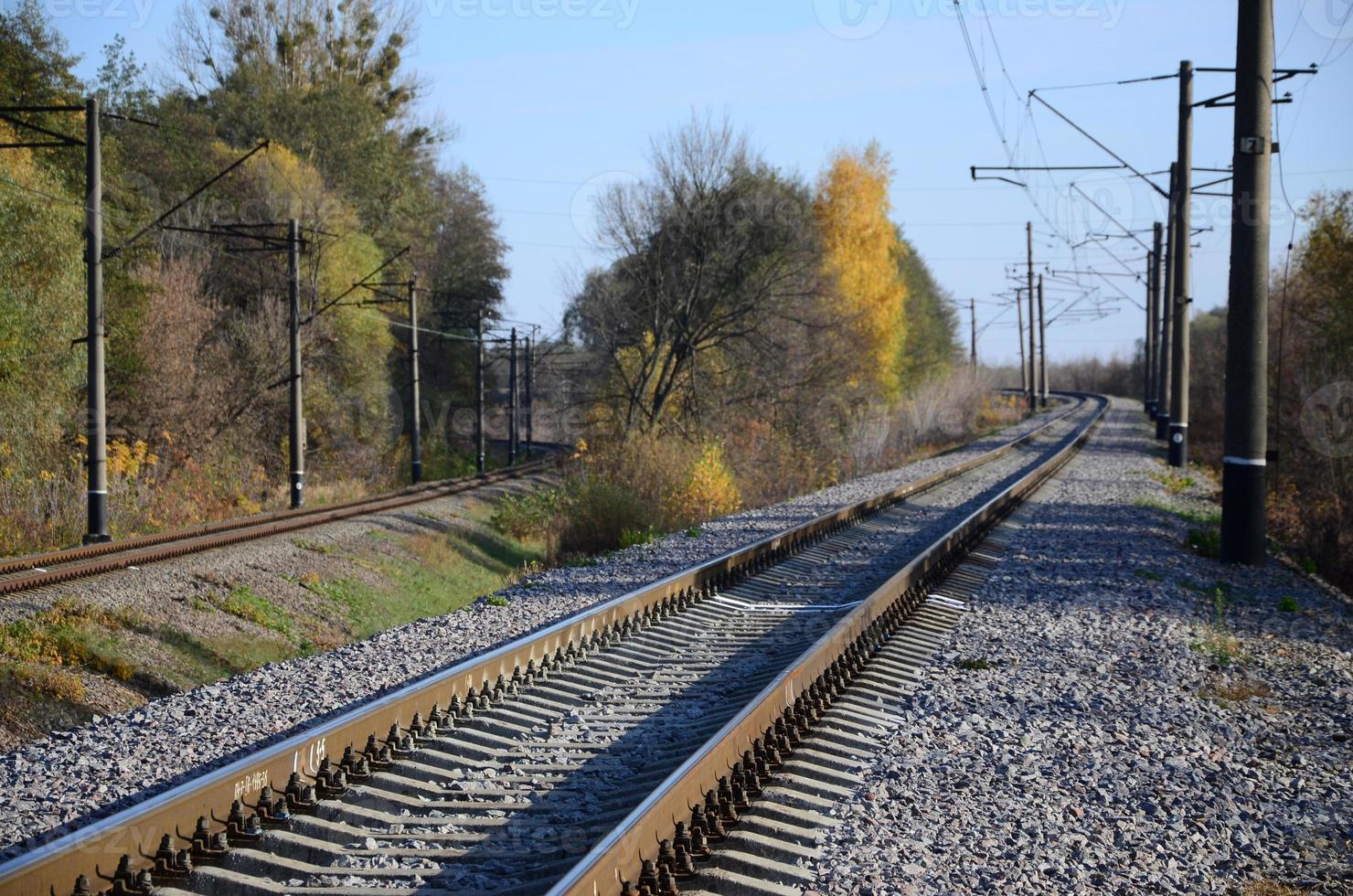 Autumn industrial landscape. Railway receding into the distance among green and yellow autumn trees photo