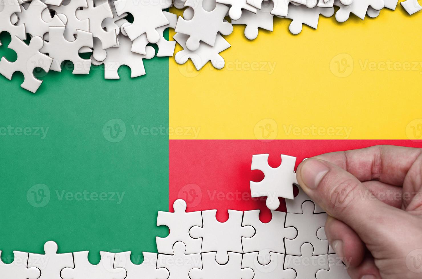 Benin flag is depicted on a table on which the human hand folds a puzzle of white color photo