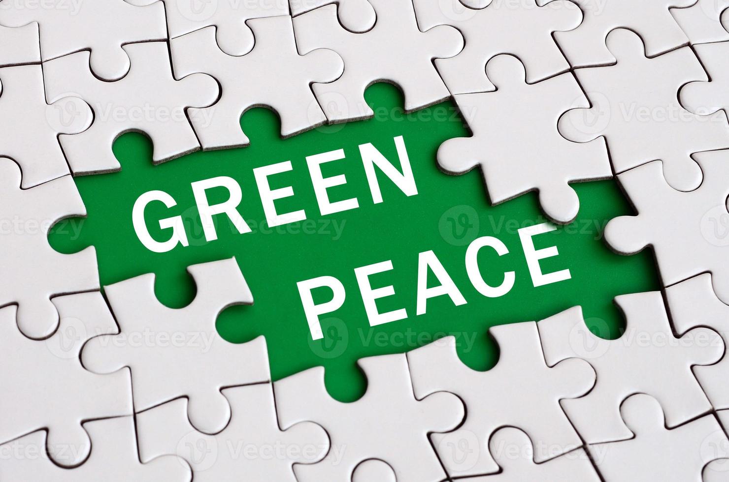 White jigsaw puzzle in assembled state with missing elements forming a green space with white inscription. Green peace photo
