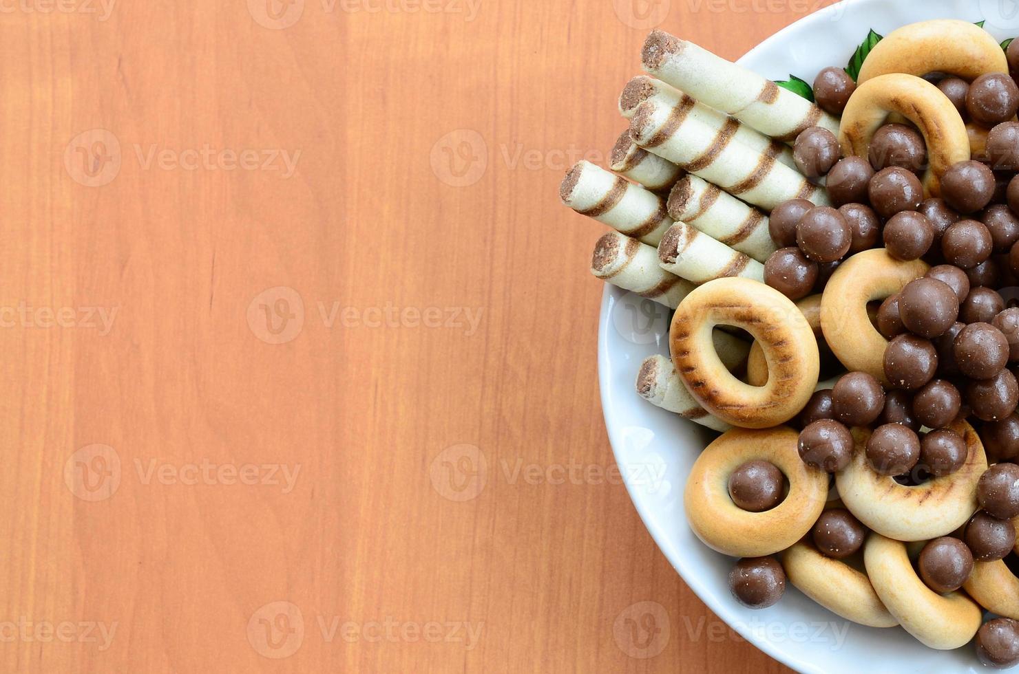Crispy tubules, chocolate melting balls and bagels lie in a white plate on a wooden table. Mix of various sweets photo