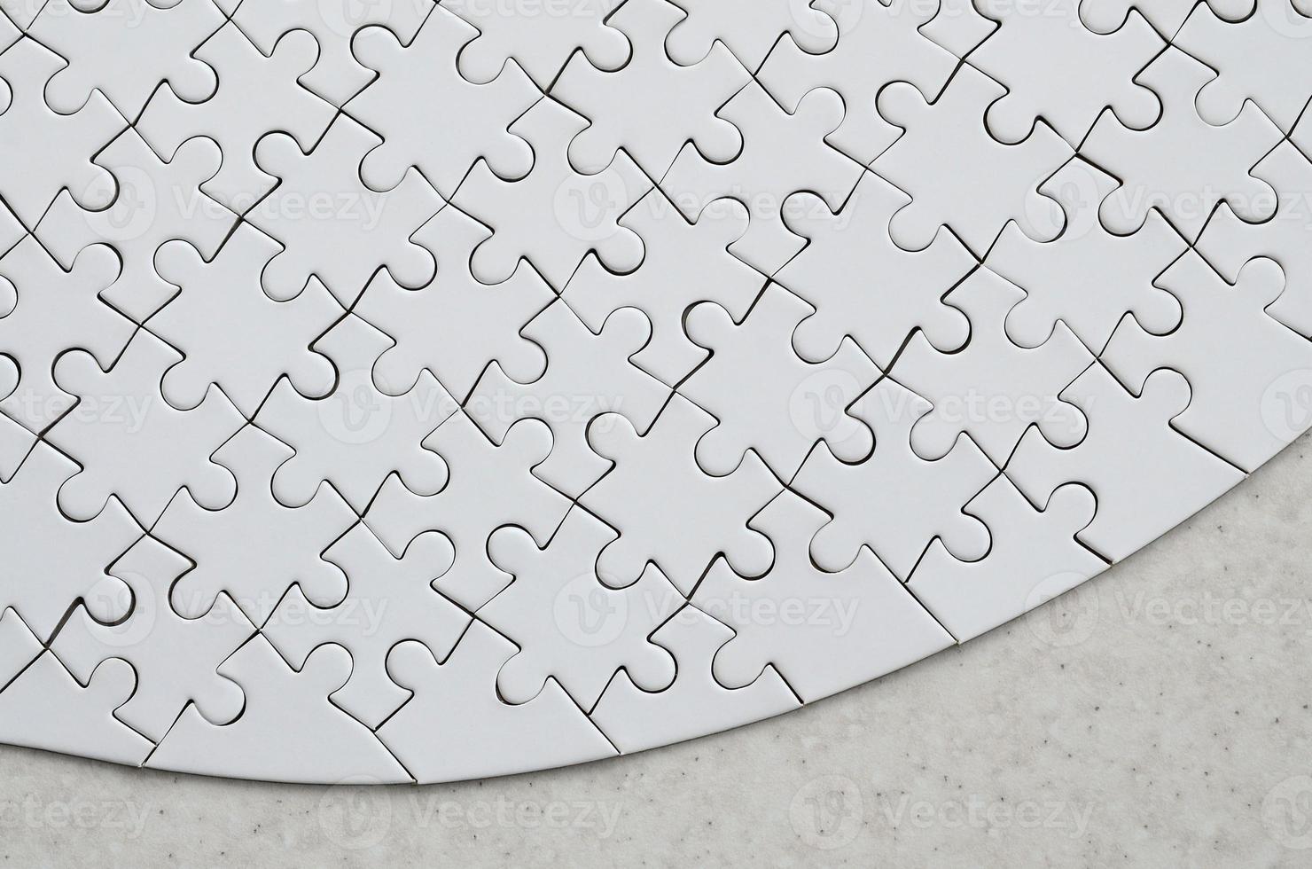 A white jigsaw puzzle in the complete form lies on a treated stone surface. Textured image with copy space photo