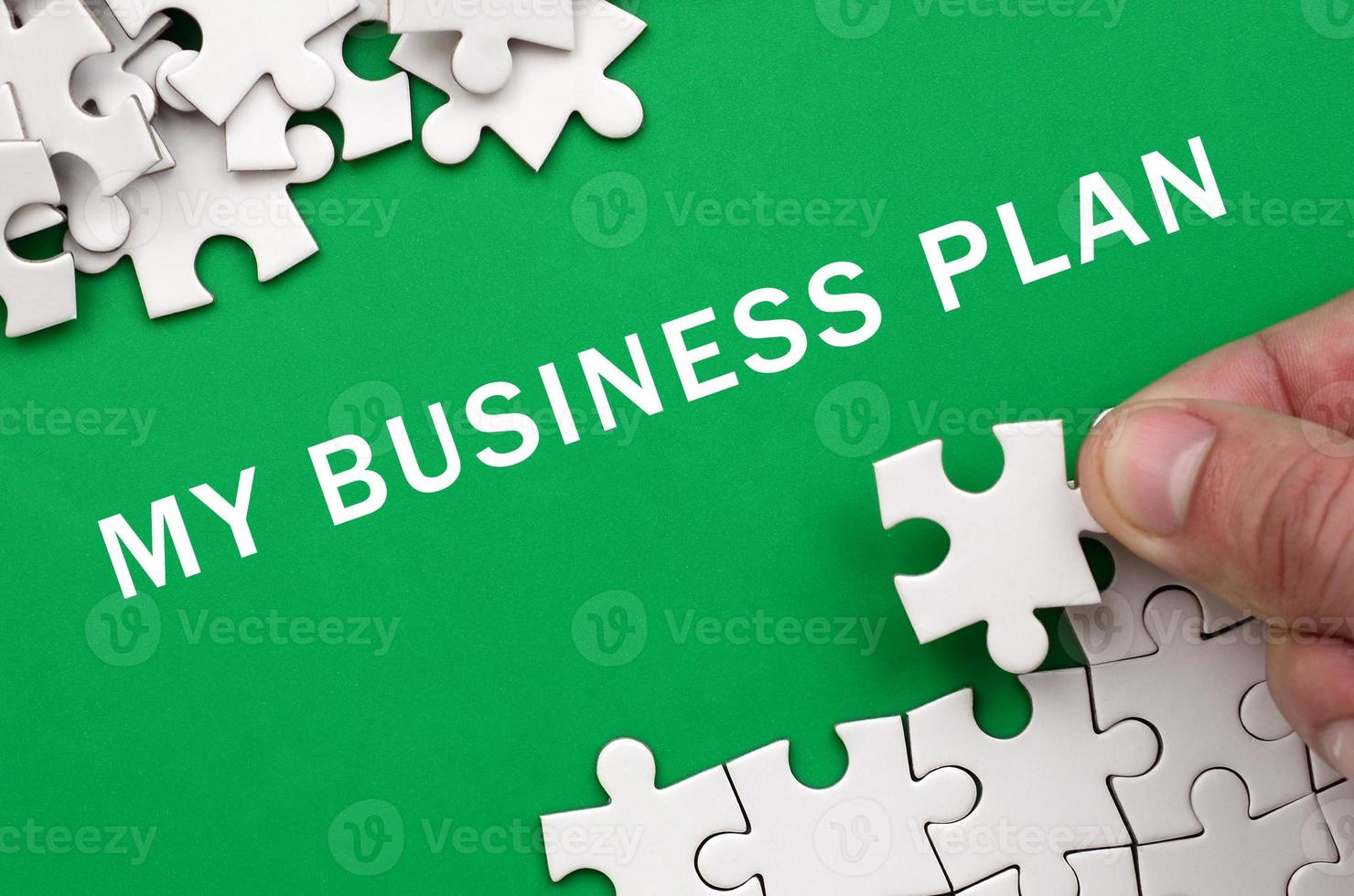 My business plan. The hand folds a white jigsaw puzzle and a pile of uncombed puzzle pieces lies against the background of the green surface photo