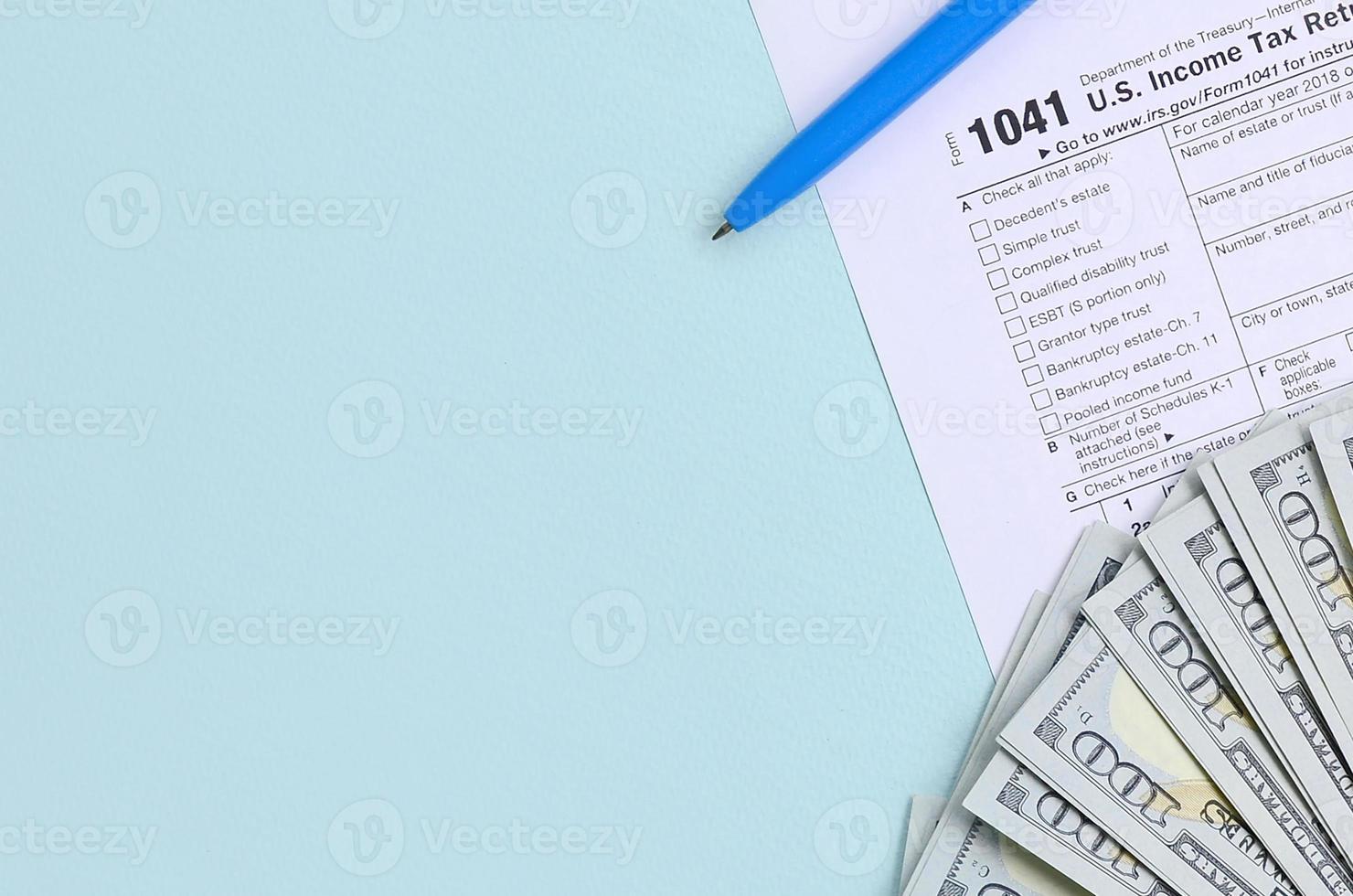 El formulario de impuestos 1041 se encuentra cerca de los billetes de cien dólares y el bolígrafo azul sobre un fondo azul claro. declaración de impuestos sobre la renta de estados unidos para sucesiones y fideicomisos foto