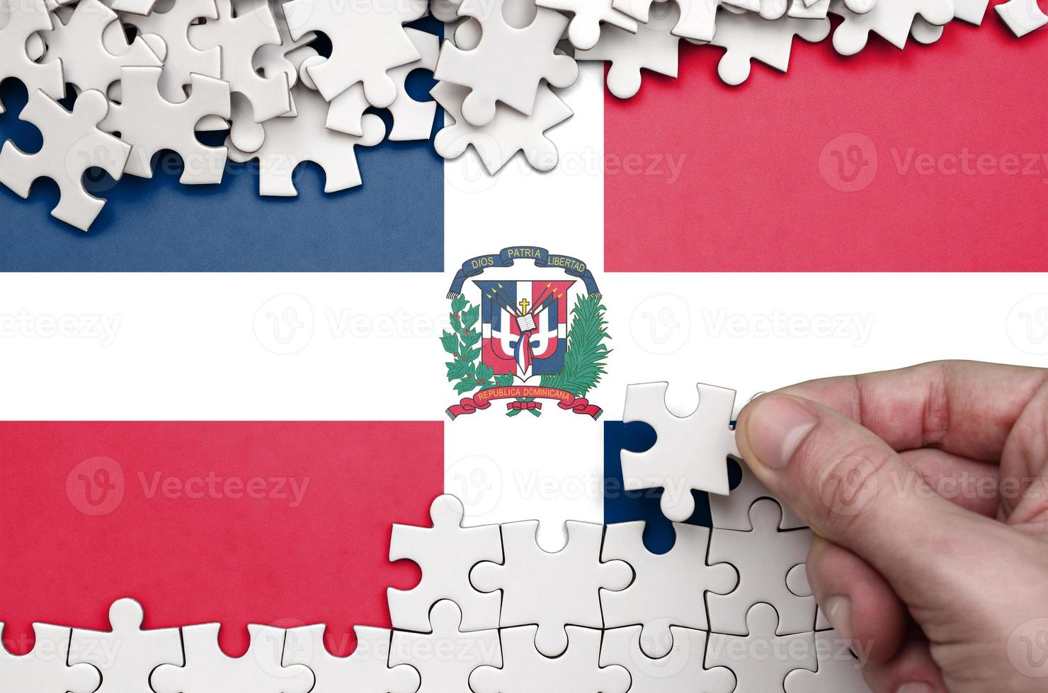 Dominican Republic flag is depicted on a table on which the human hand folds a puzzle of white color photo