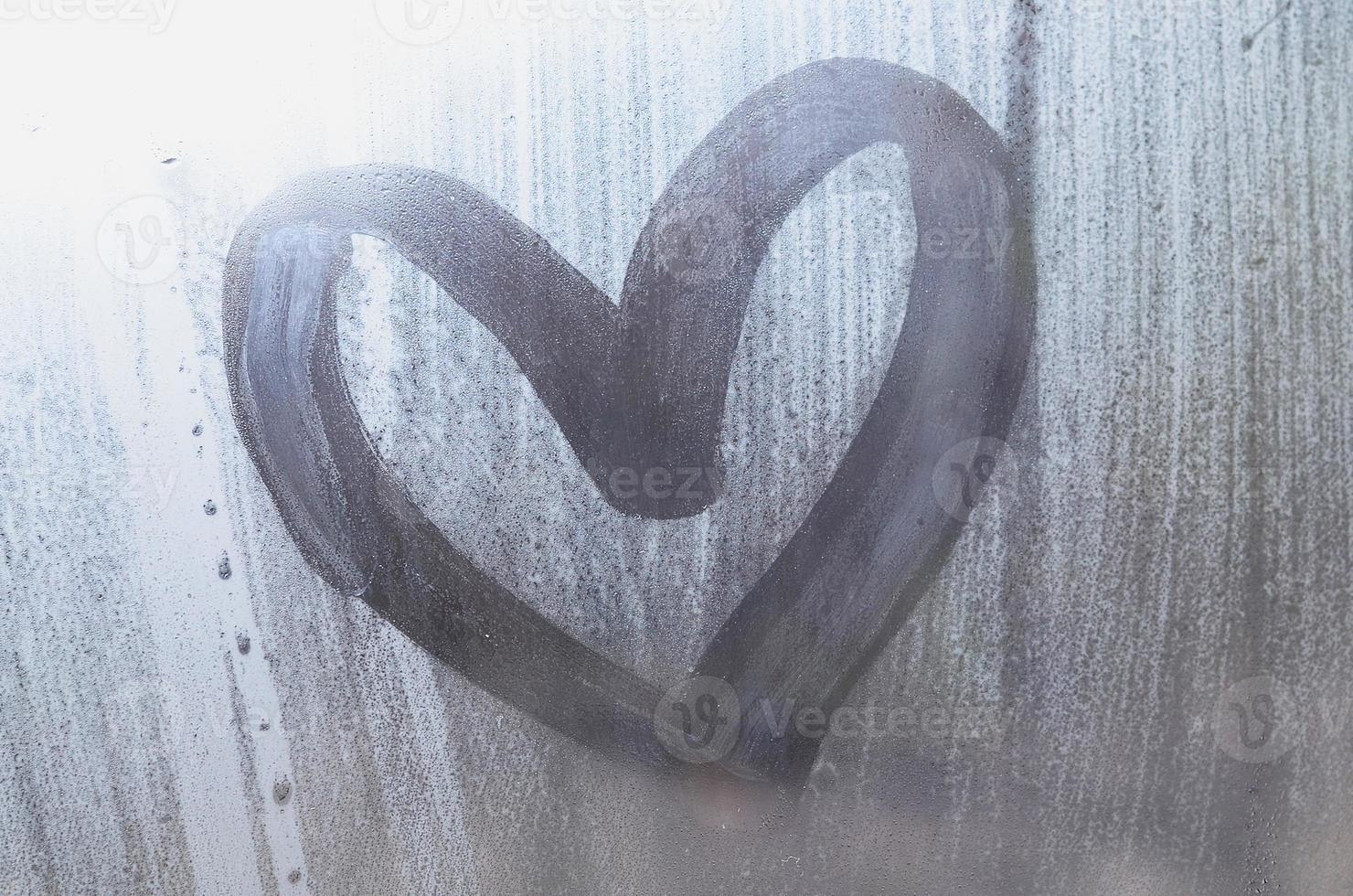 A heart-shaped drawing drawn by a finger on a misted glass in rainy weather photo