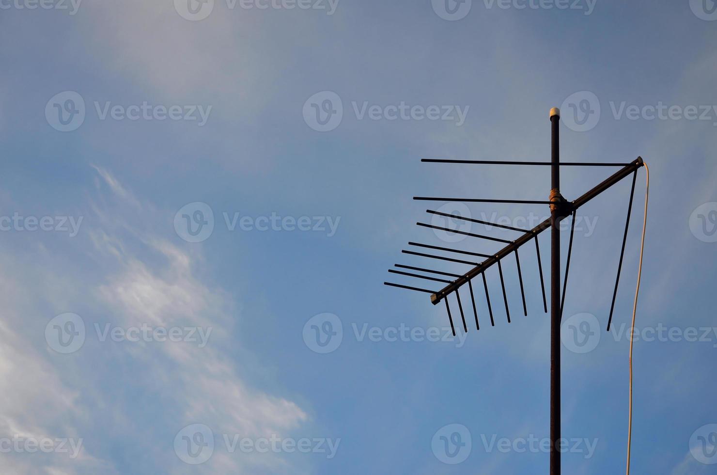 An old and rusty television antenna against a cloudy blue sky photo