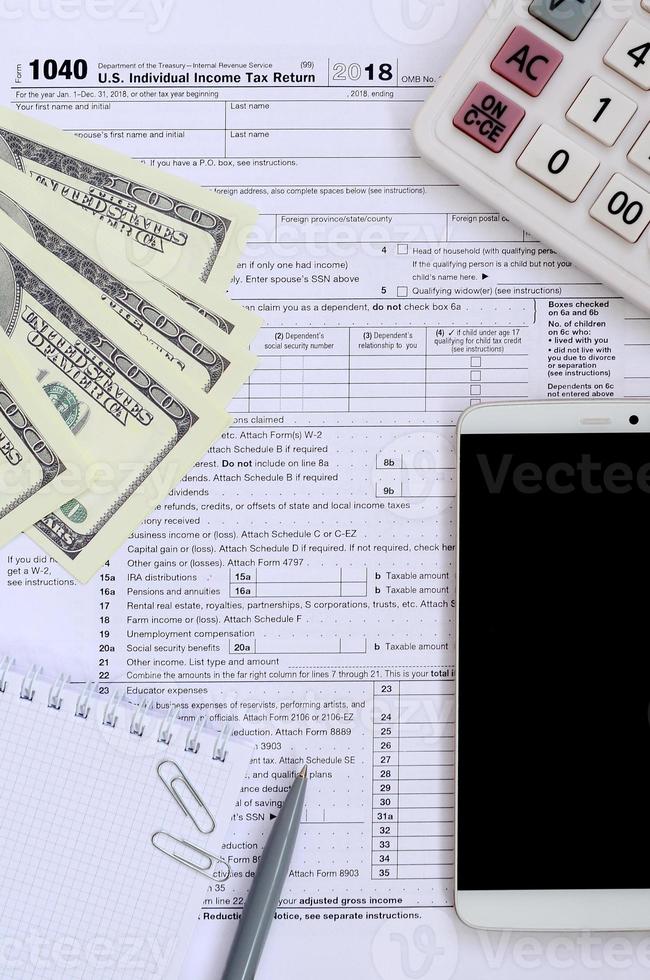 Composition of items lying on the 1040 tax form. Dollar bills, pen, calculator, smartphone, paper clip and notepad. The time to pay taxes photo