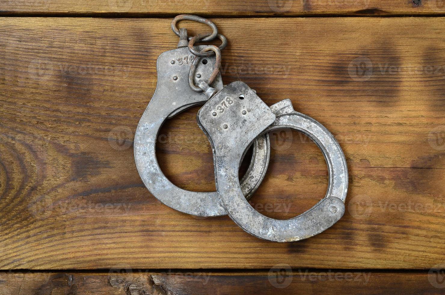 Old and rusty police handcuffs lie on a scratched wooden surface. The concept of an old crime photo