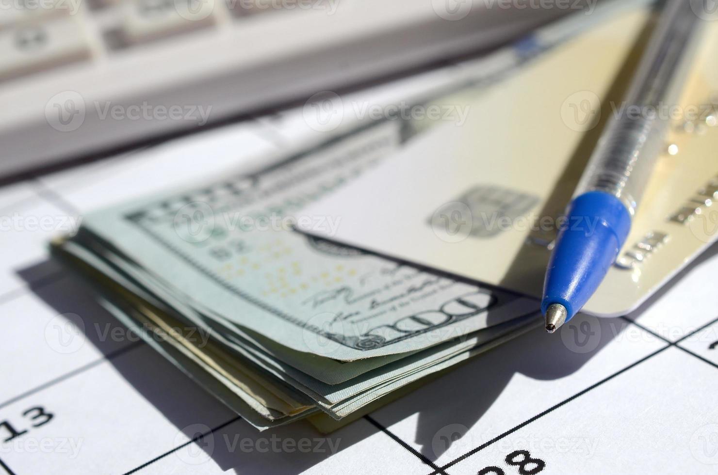 Pen and credit card on many hundred US dollar bills and calculator on calendar page close up photo