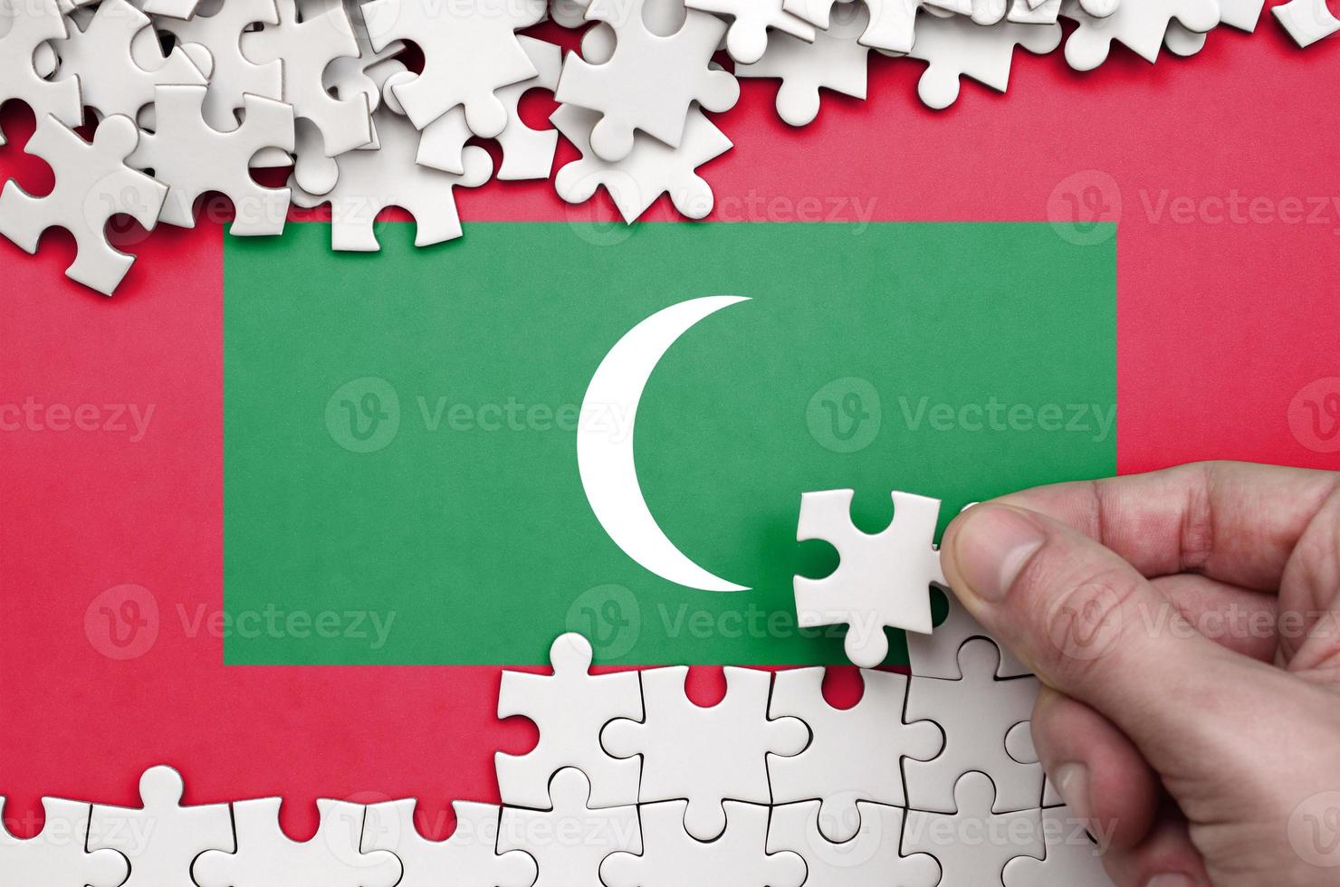 Maldives flag is depicted on a table on which the human hand folds a puzzle of white color photo