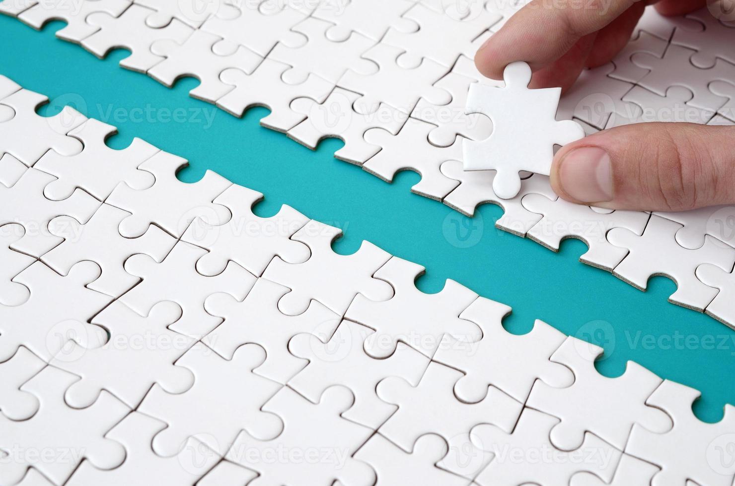 The human hand paves the way to the surface of the jigsaw puzzle, forming a blue space. The concept of overcoming the difficulties on the way to success photo