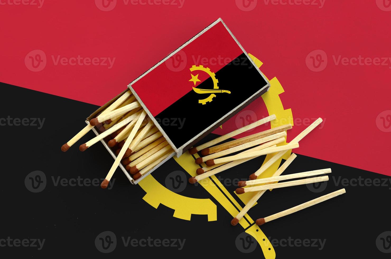 Angola flag is shown on an open matchbox, from which several matches fall and lies on a large flag photo