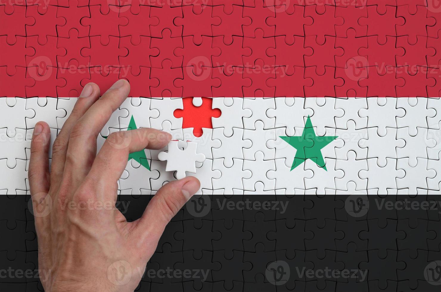 Syria flag is depicted on a puzzle, which the man's hand completes to fold photo