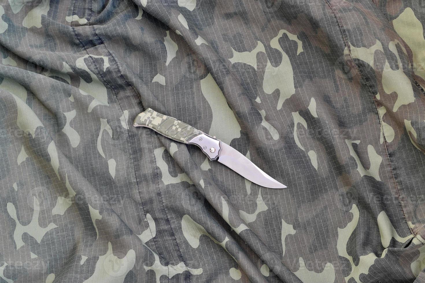Military knife on army camouflage clothes close up. Background with copy space for military or special service design photo