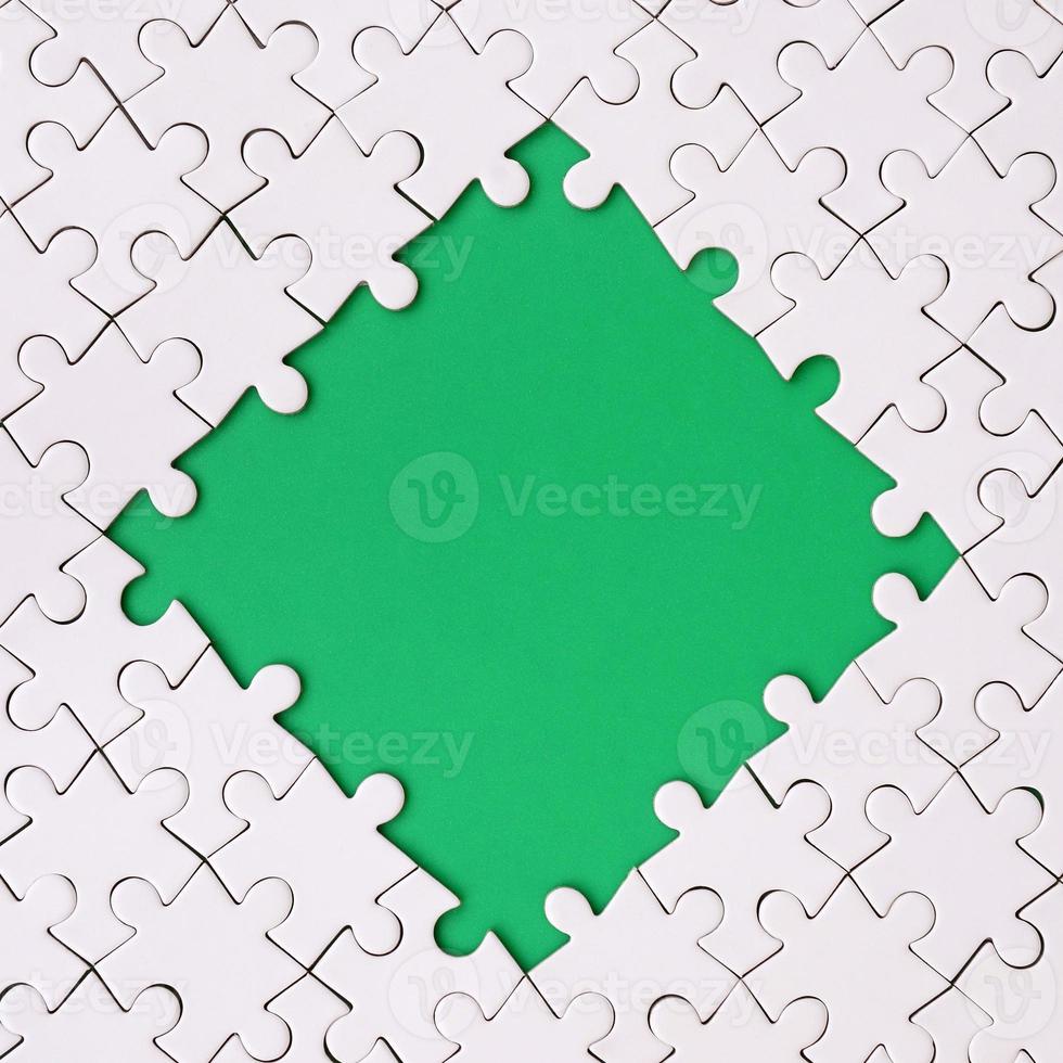 Framing in the form of a rhombus, made of a white jigsaw puzzle around the green space photo