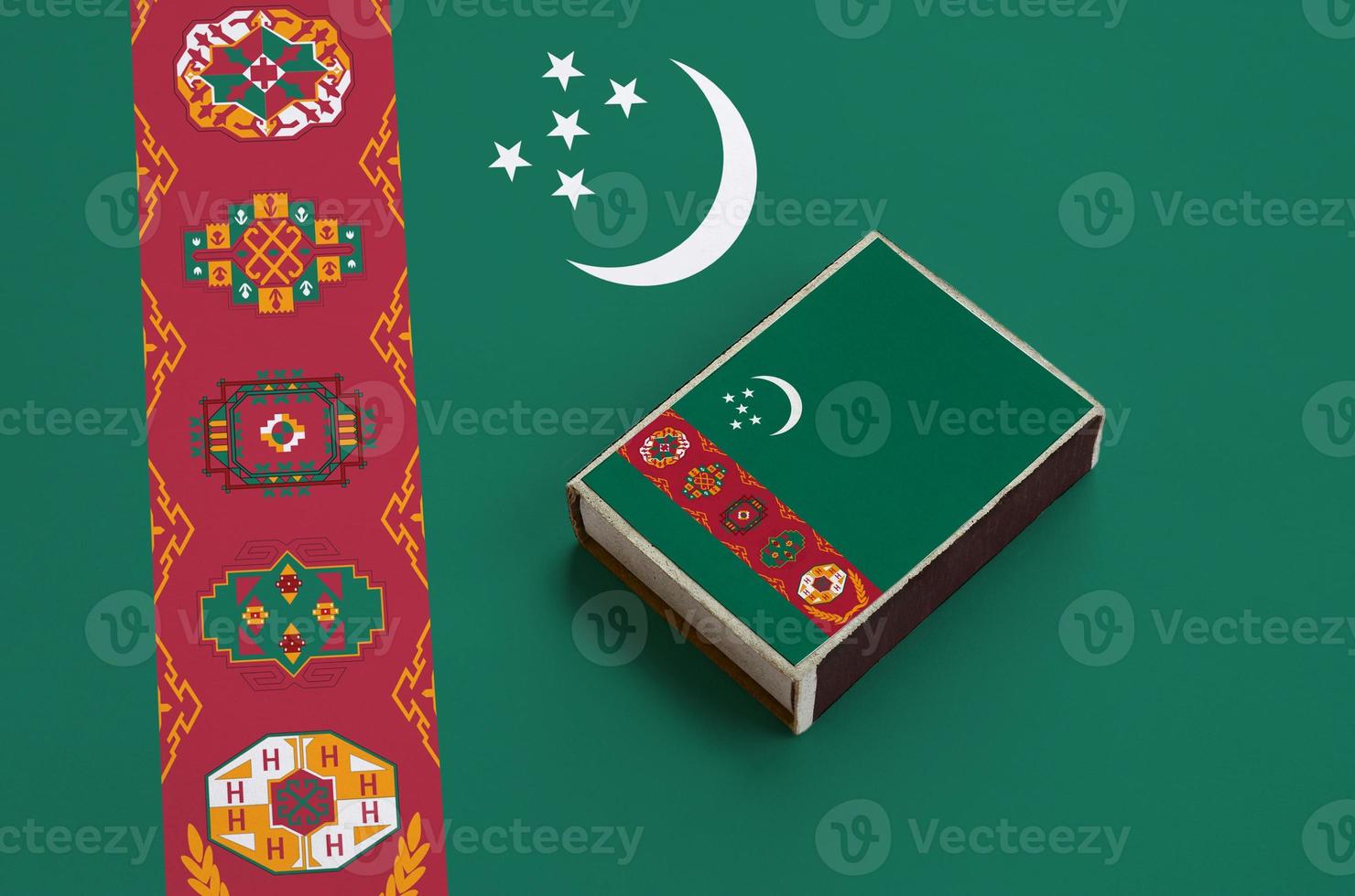 Turkmenistan flag is pictured on a matchbox that lies on a large flag photo