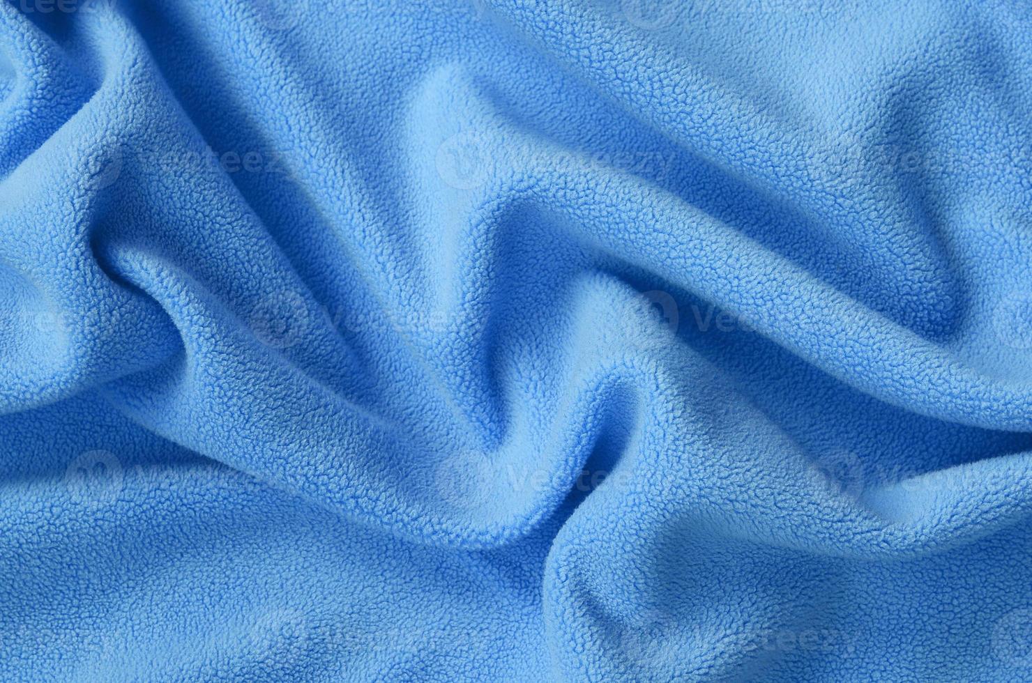 The blanket of furry blue fleece fabric. A background of light blue soft plush fleece material with a lot of relief folds photo
