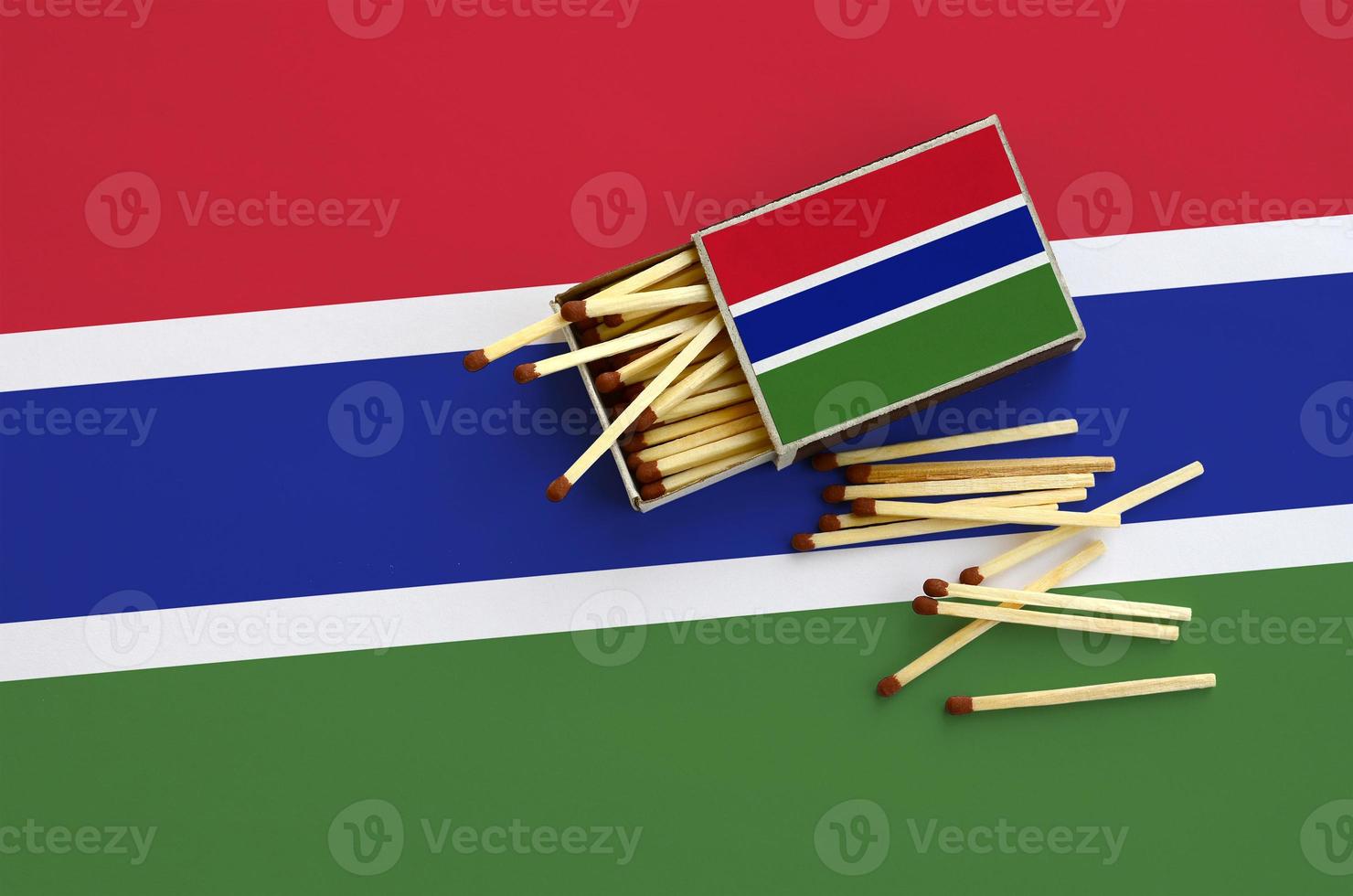Gambia flag is shown on an open matchbox, from which several matches fall and lies on a large flag photo