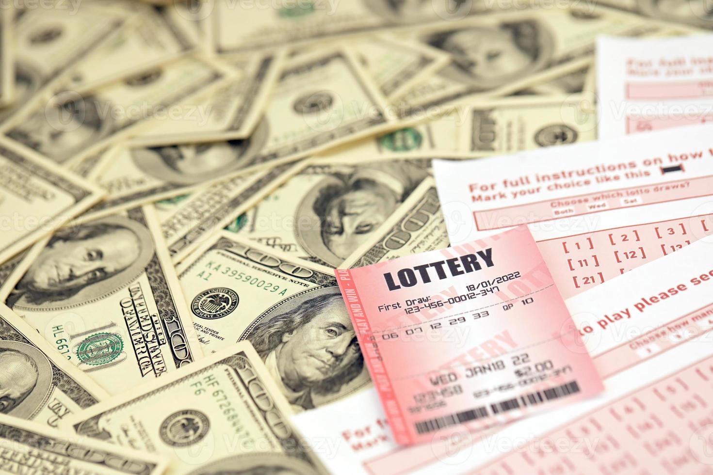 el billete de lotería rojo se encuentra en hojas de juego rosas con números para marcar en una gran cantidad de billetes de cien dólares. concepto de juego de lotería o adicción al juego. de cerca foto
