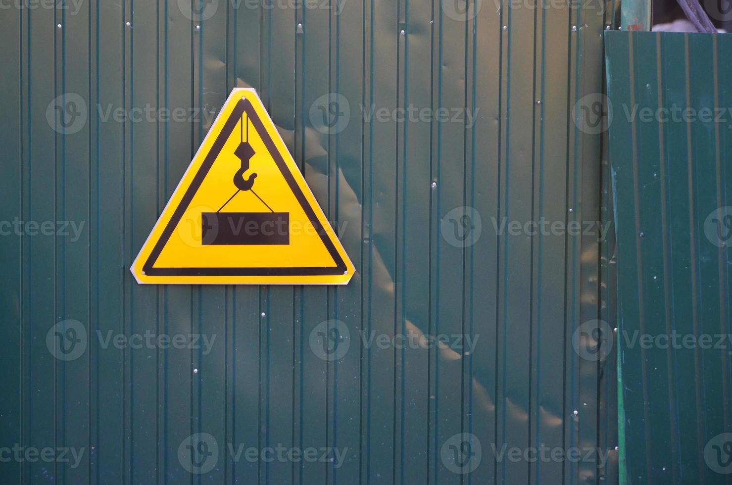 Traffic sign with a picture of a large and heavy square slab hanging from a lifting crane cable. Construction work is underway photo